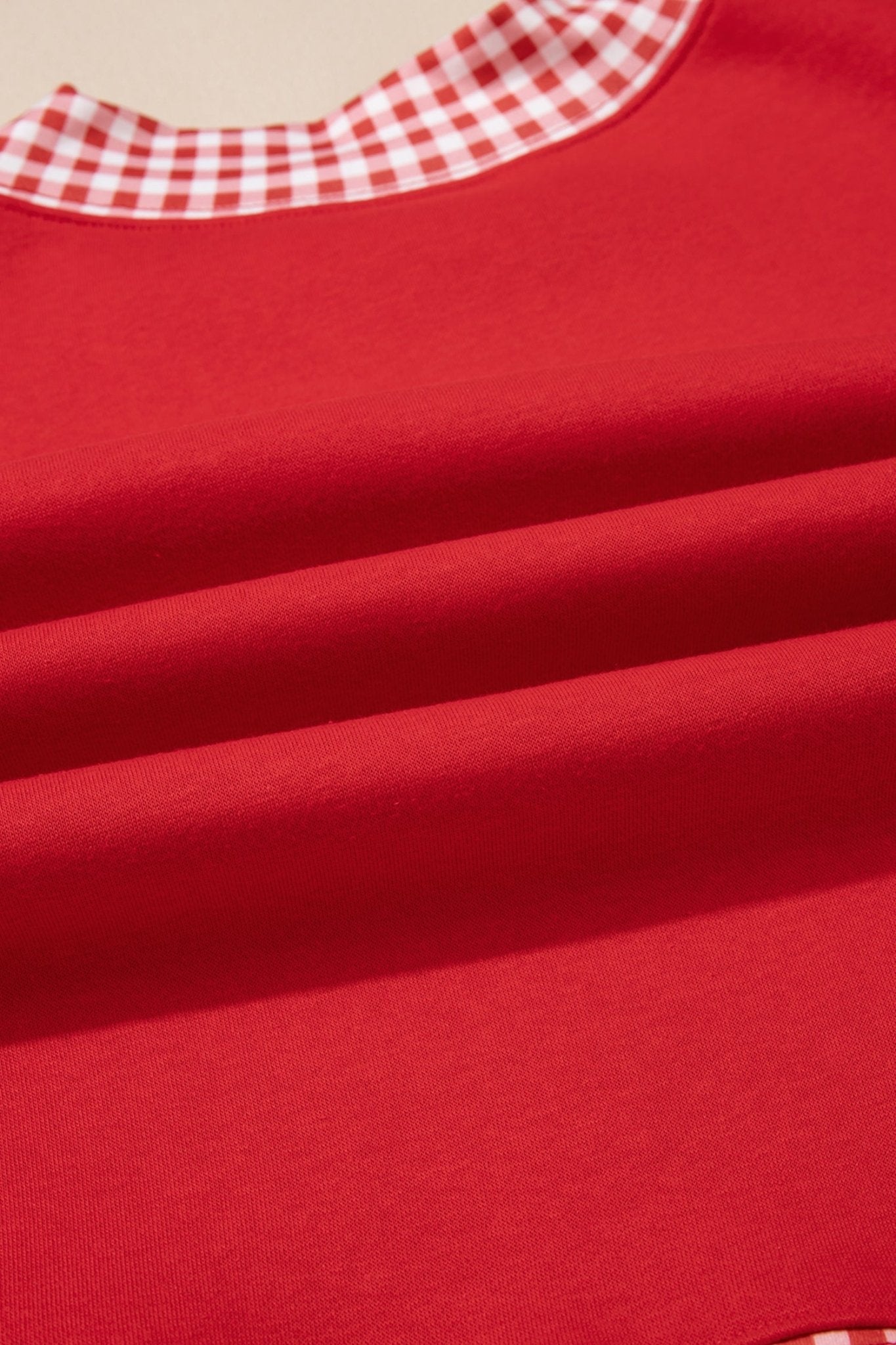 A close-up of a bright red garment, likely a baby bib or top, featuring a red and white gingham checkered collar.