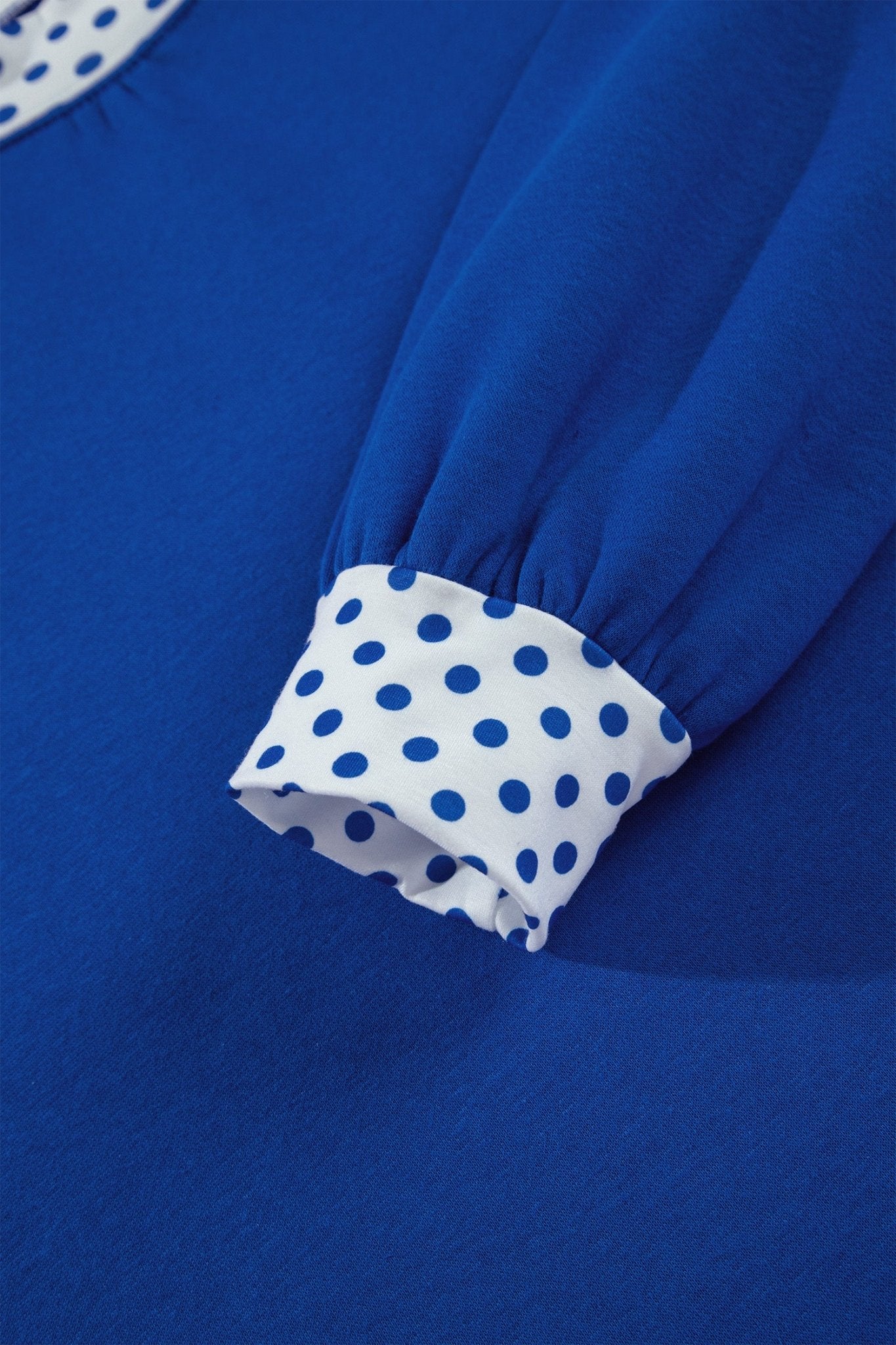 Close-up of a royal blue garment with a gathered cuff featuring a white and blue polka dot pattern.