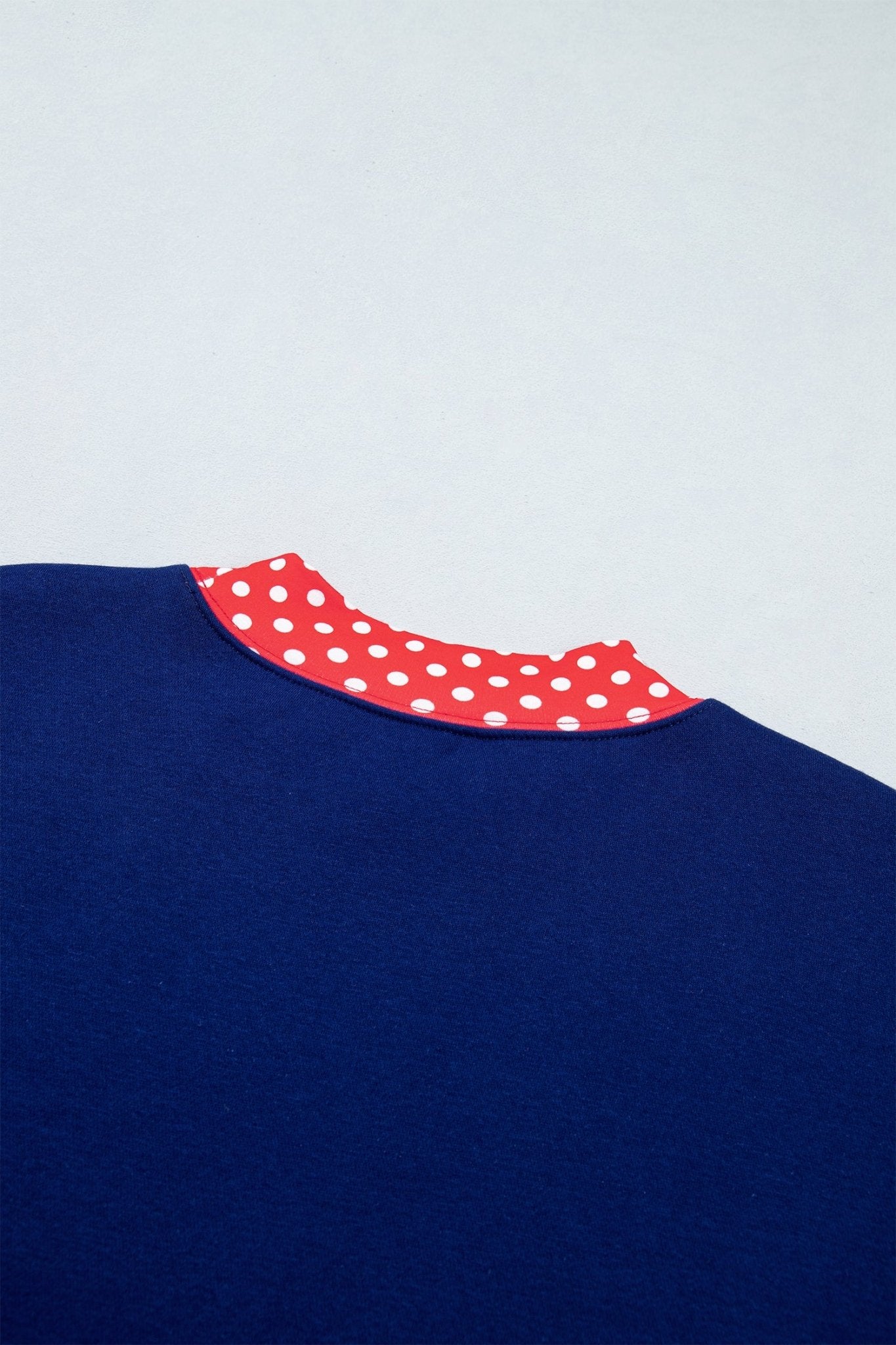 Close-up of navy blue garment with contrasting red collar featuring white polka dots on light gray.
