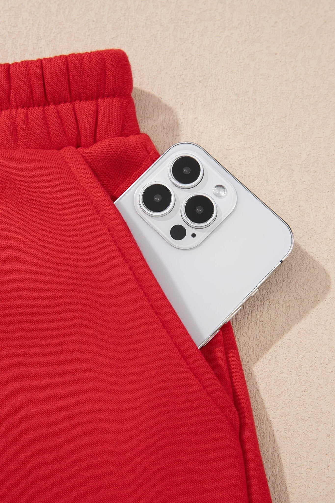 Close-up of bright red sweatshirt pocket holding a silver smartphone against a light beige textured background.