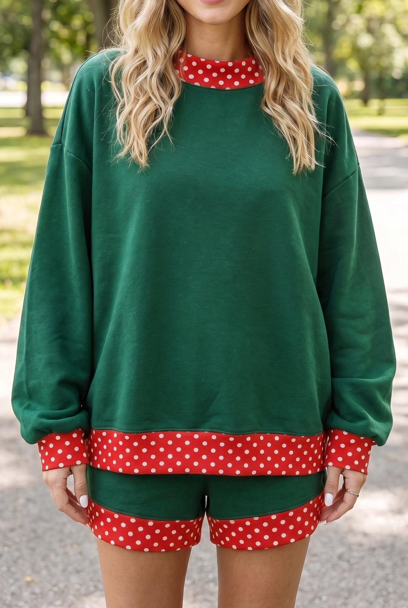 Woman wearing green long-sleeve sweatshirt and matching shorts with red-white polka-dot trim outdoors.