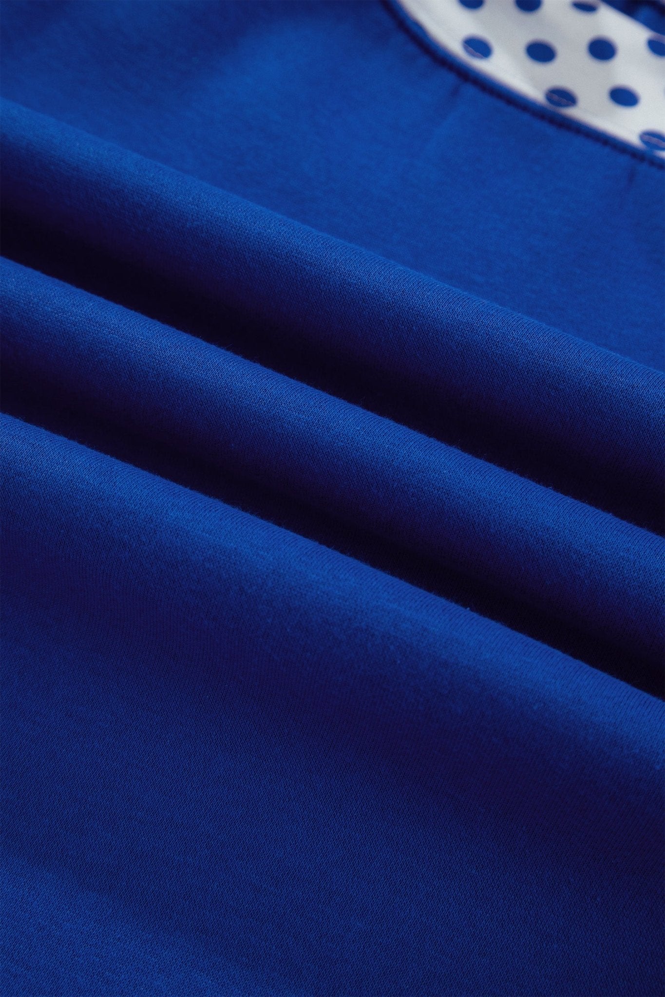 Close-up of royal blue fabric with soft folds and texture, with white polka-dot fabric visible at top right.