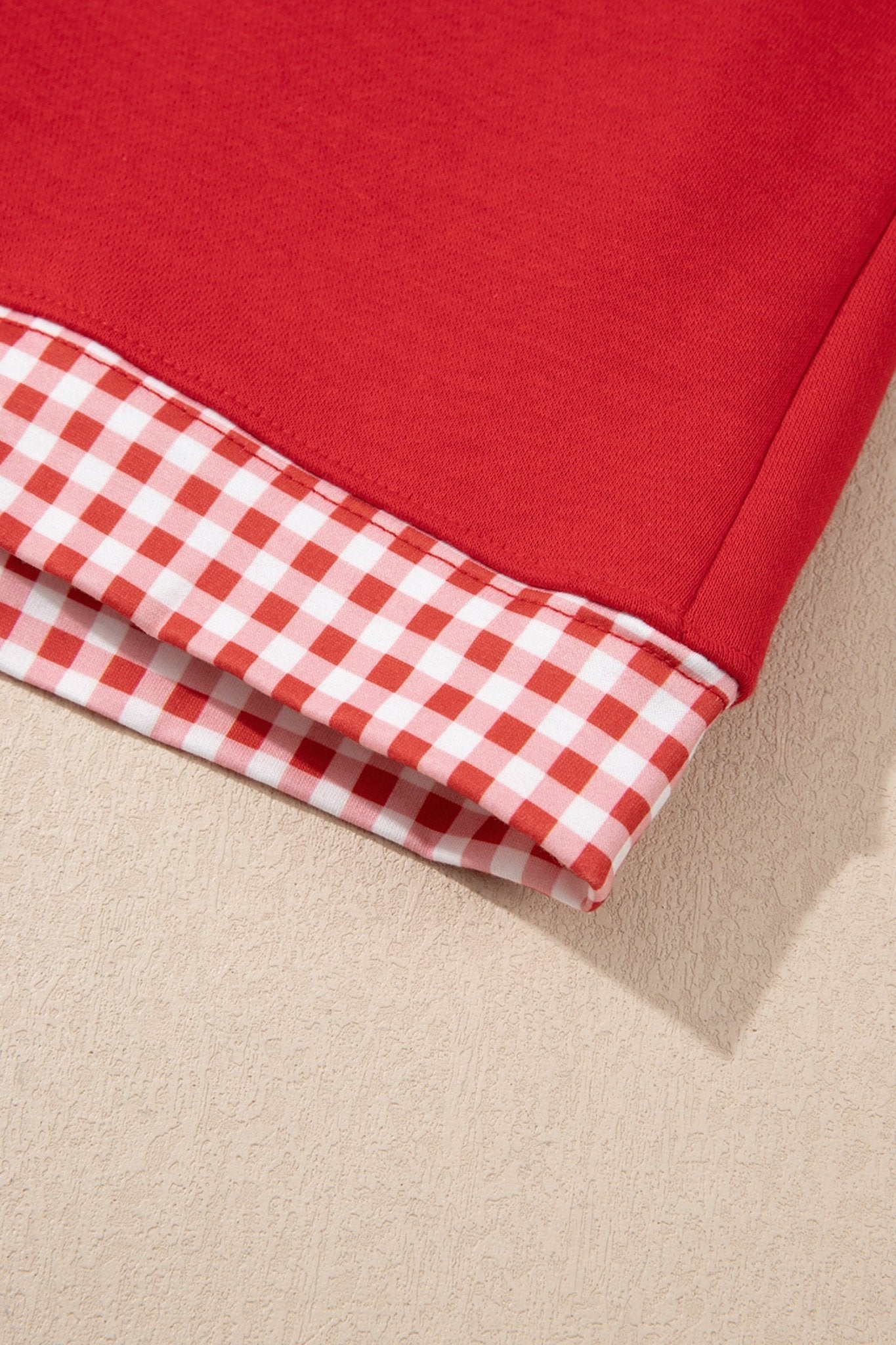 Close-up of folded red garment showing red-white gingham check lining on a light beige textured surface.