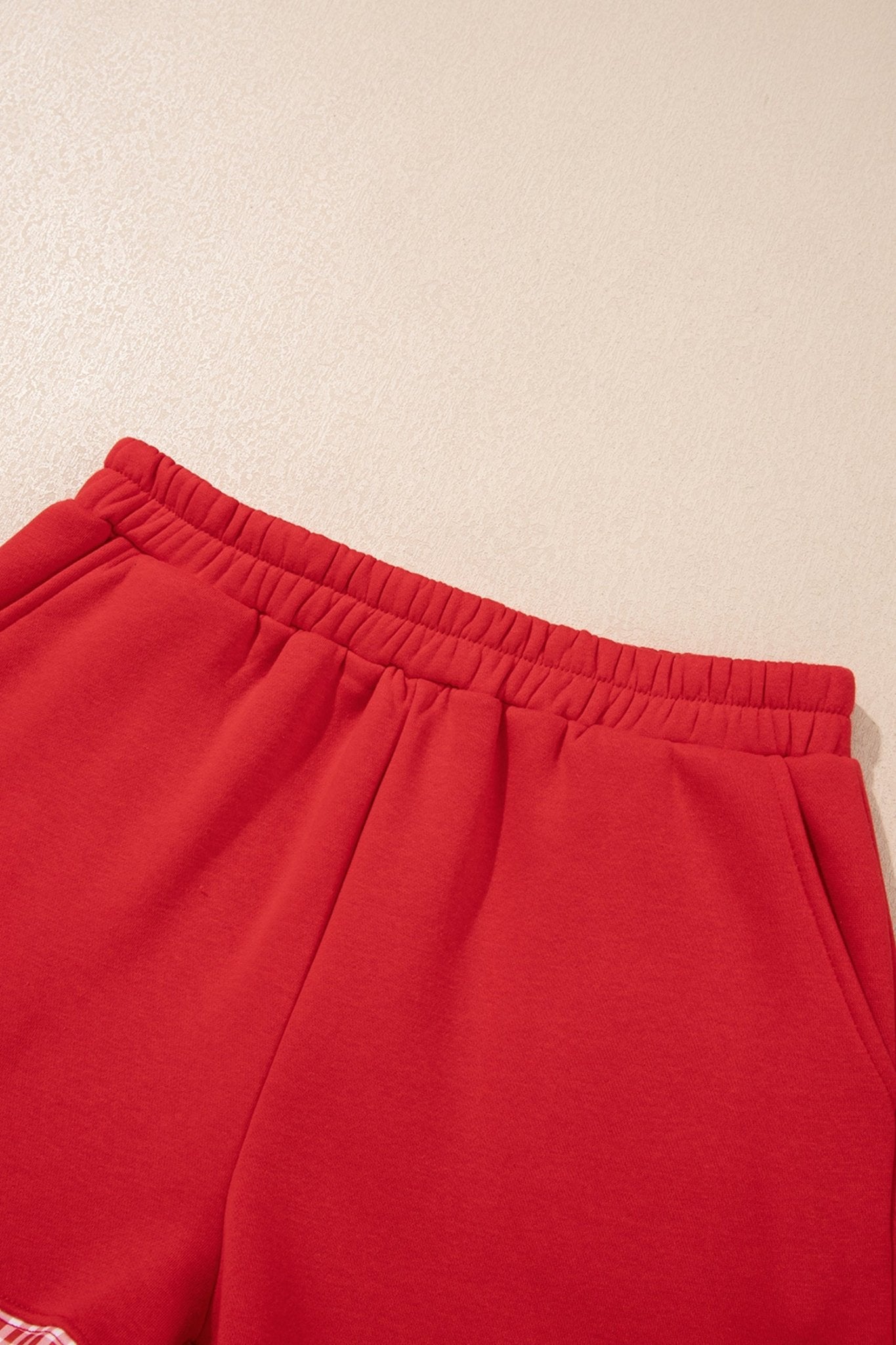 Close-up of bright red sweatpants with elastic waistband and upper front fabric on beige.