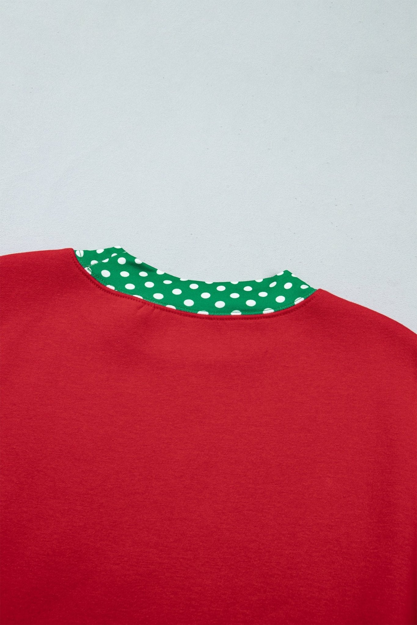 Close-up of red sweatshirt back with green-white polka-dot inner collar lining against a light gray background.