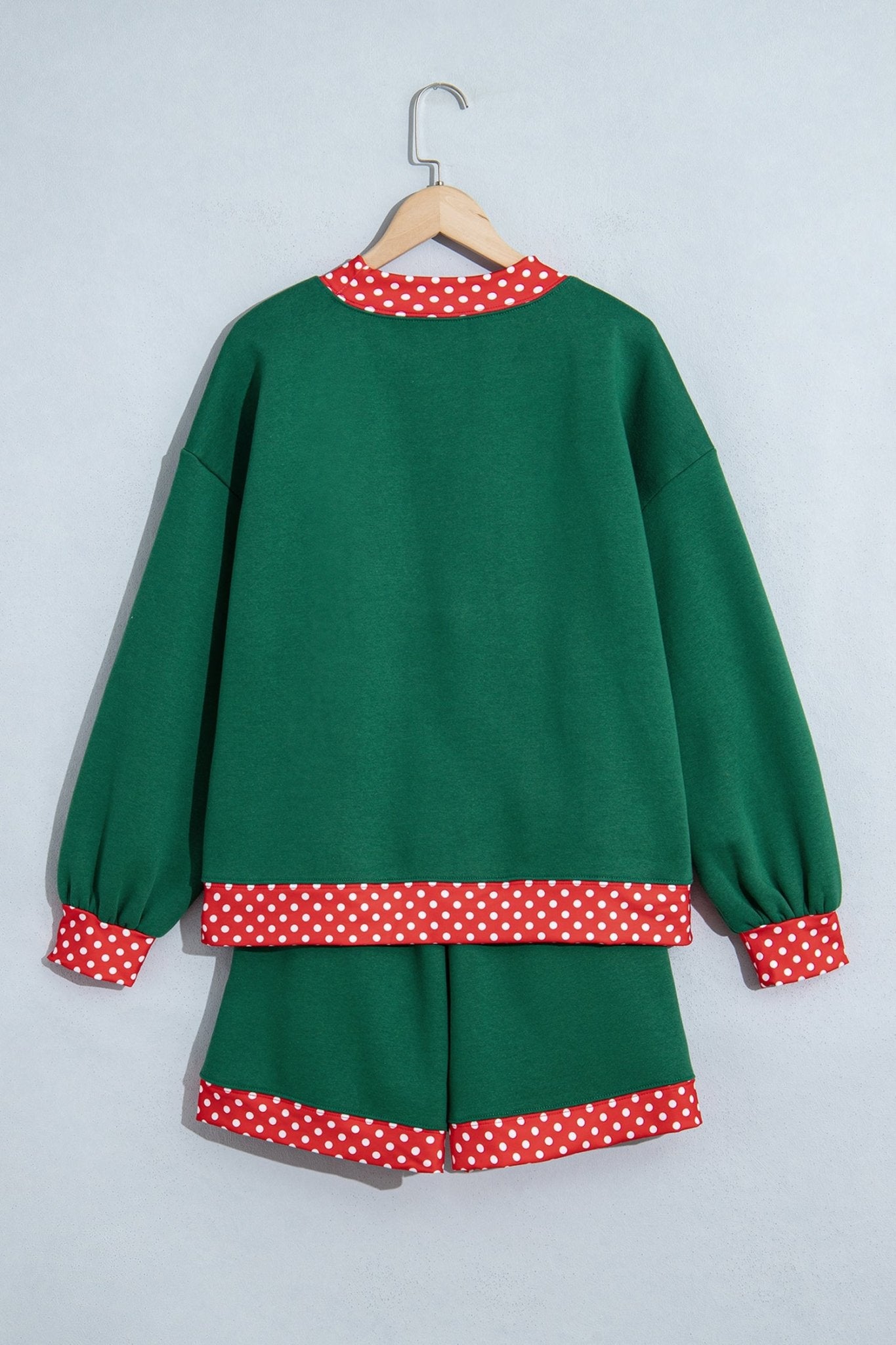 Green two-piece lounge set with sweatshirt and shorts, featuring red-white polka-dot trim, on a wooden hanger.
