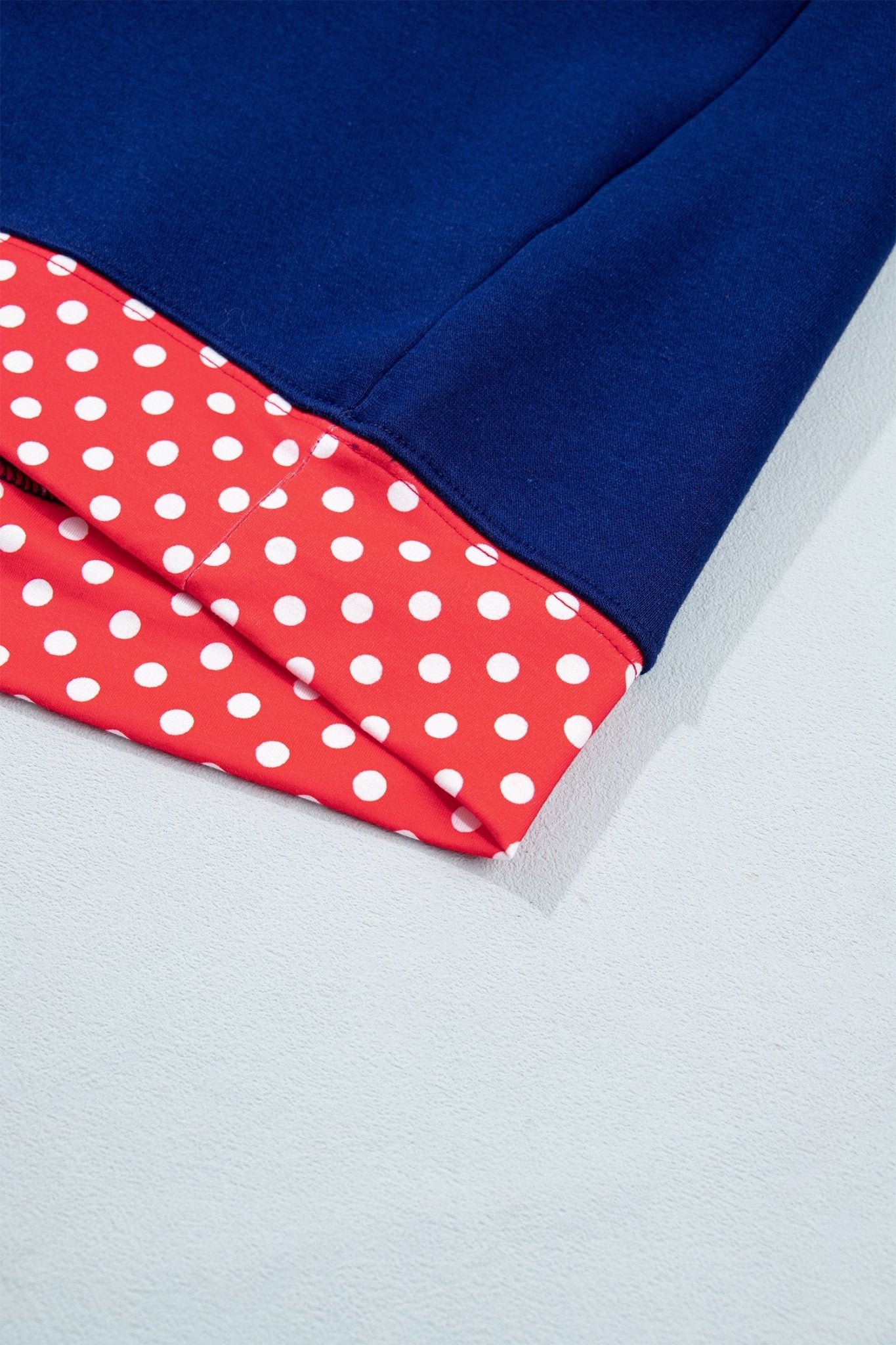 Close-up of a folded navy blue fabric item showing a red lining with white polka dots, set against a light gray background.