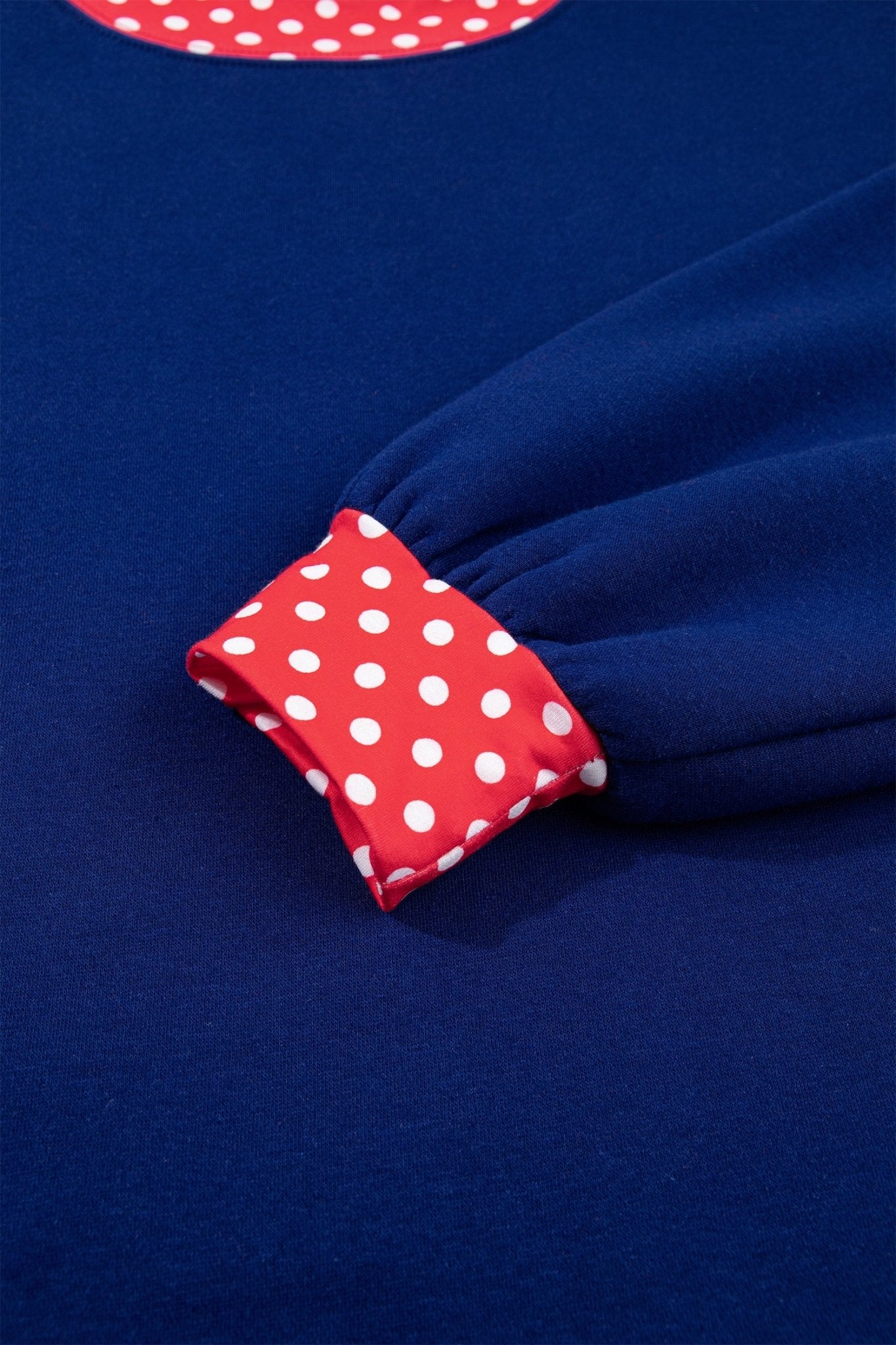 Close-up of a navy blue garment with a red and white polka dot cuff detail and a matching polka dot neckline.
