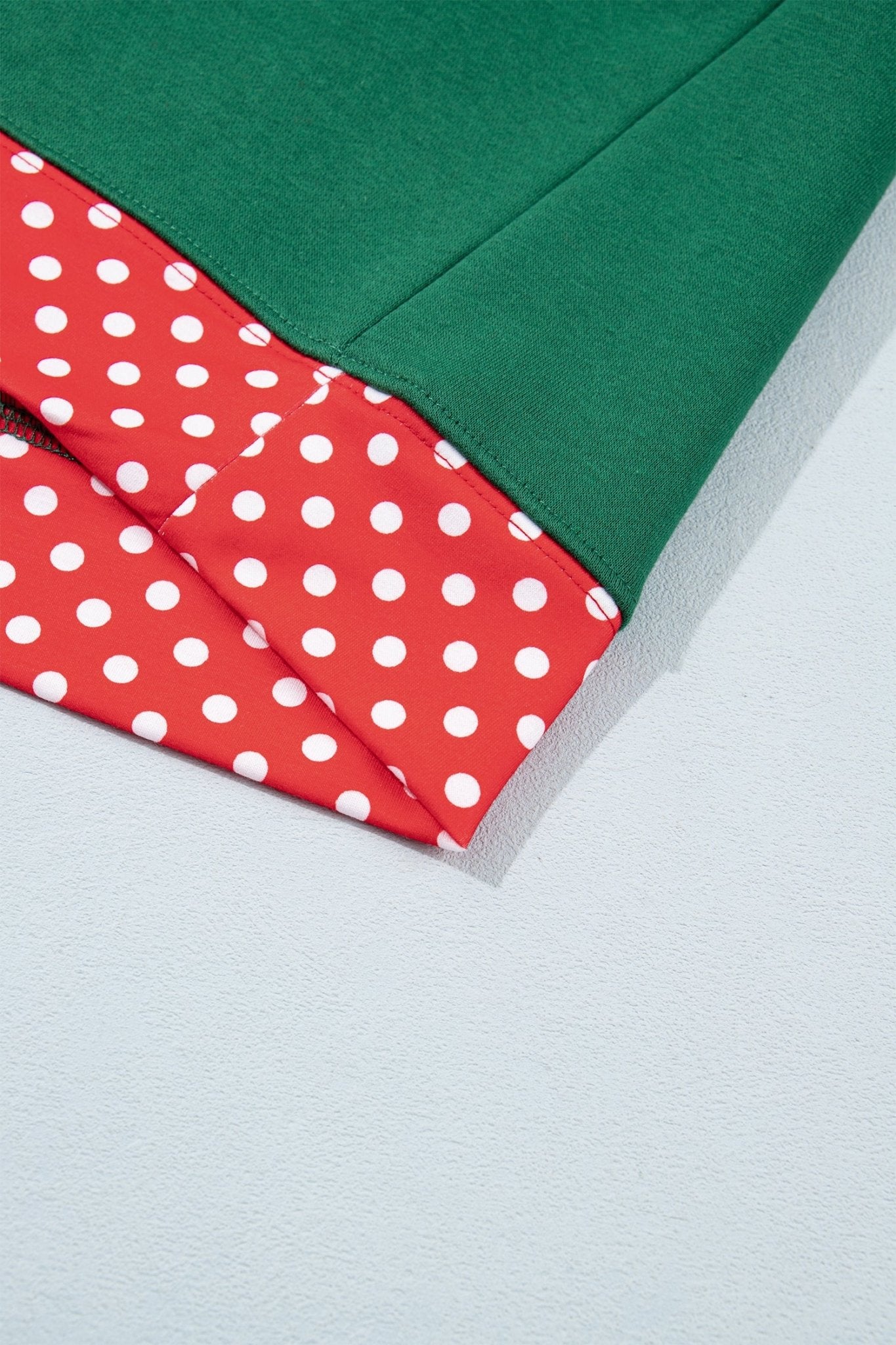 Folded textile showing solid dark green and red fabric with white polka dots on a light gray surface.