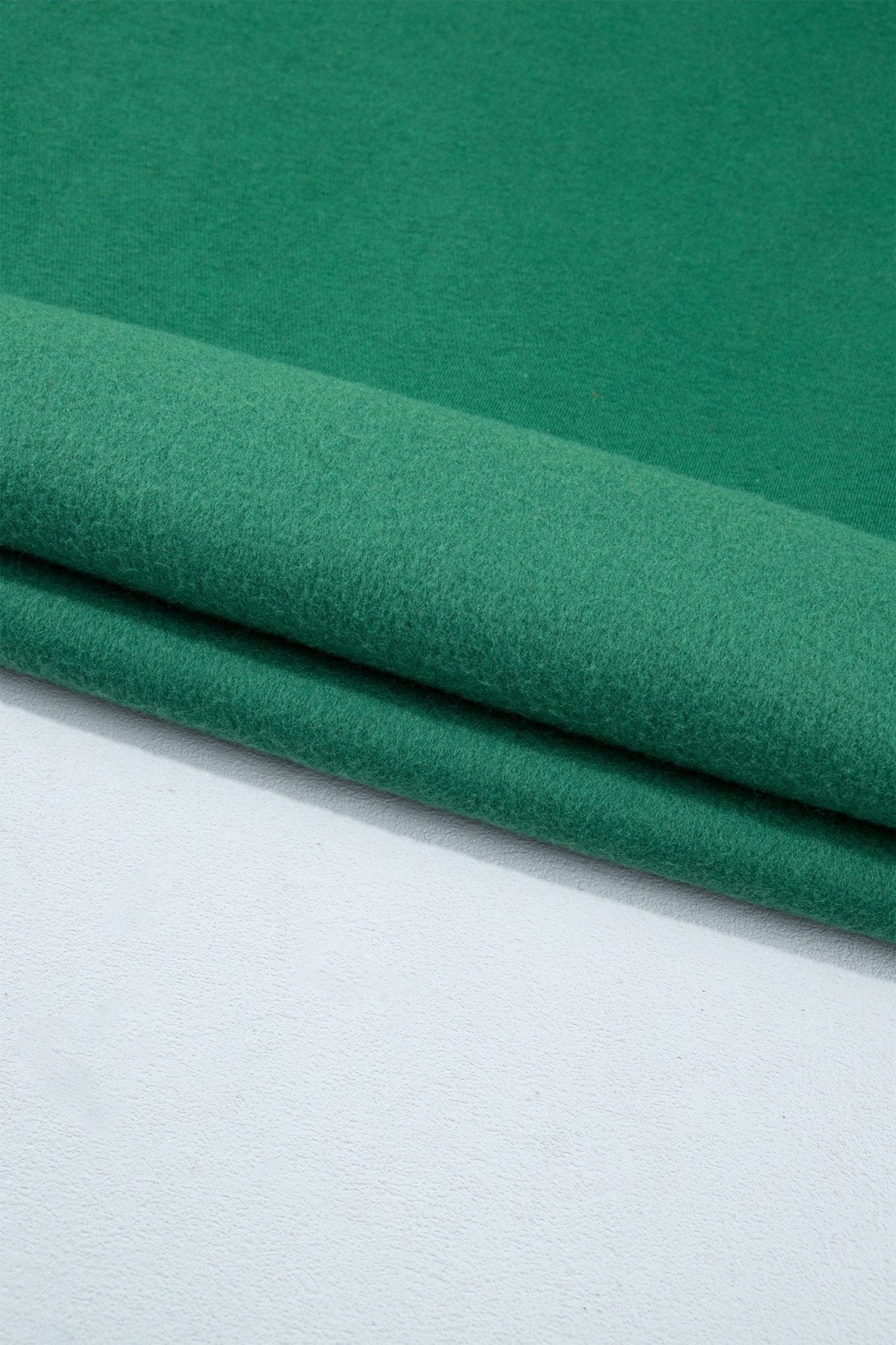 A close-up of folded green fabric resting on a white surface, showing the material texture and color.
