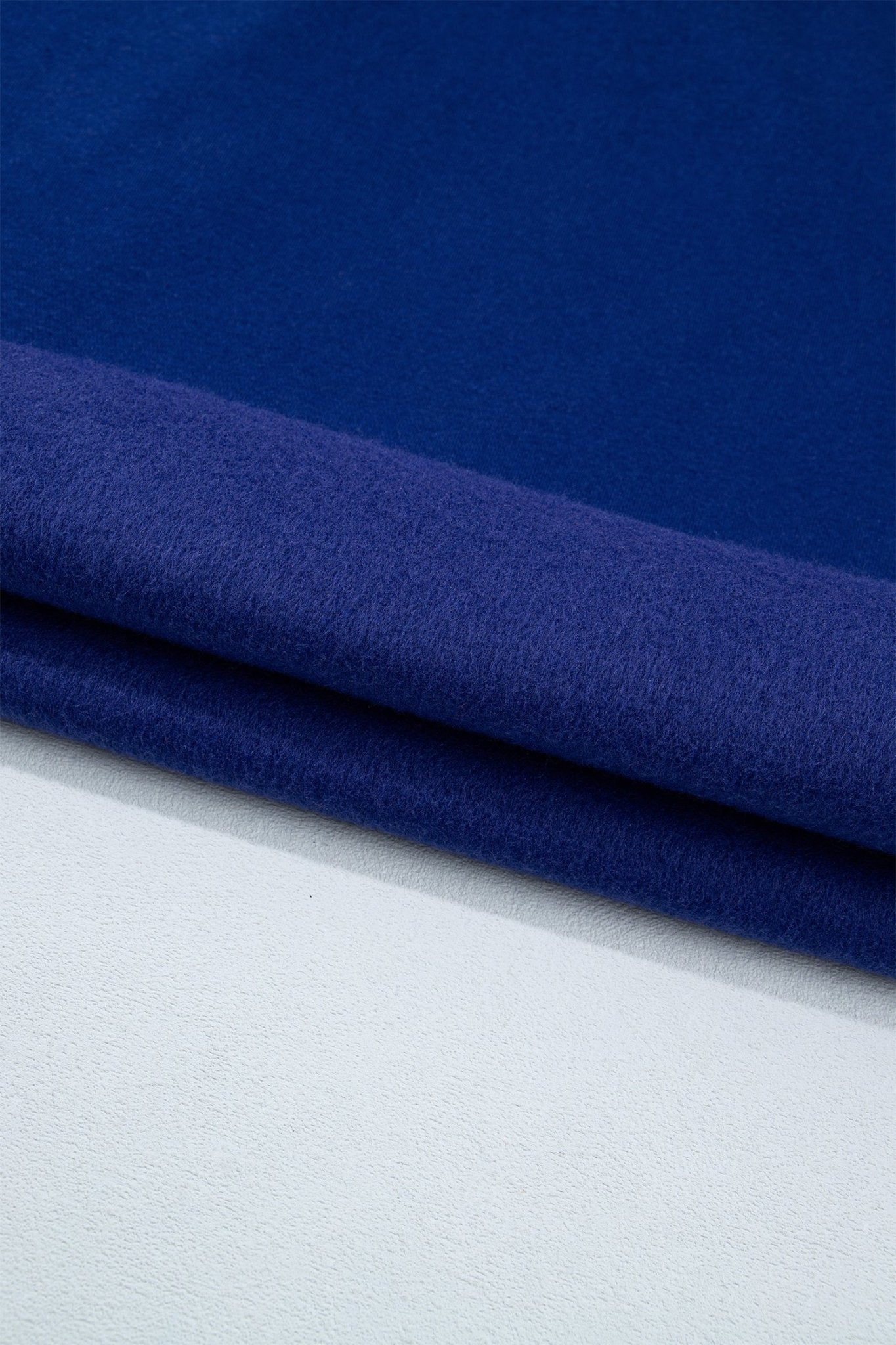 A close-up of dark navy blue fabric with soft diagonal folds showing its texture and color.