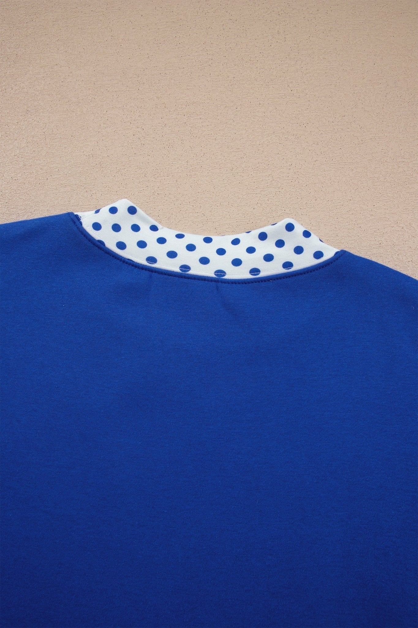 Close-up of royal blue sweatshirt back with white collar and blue polka dots against a beige background.