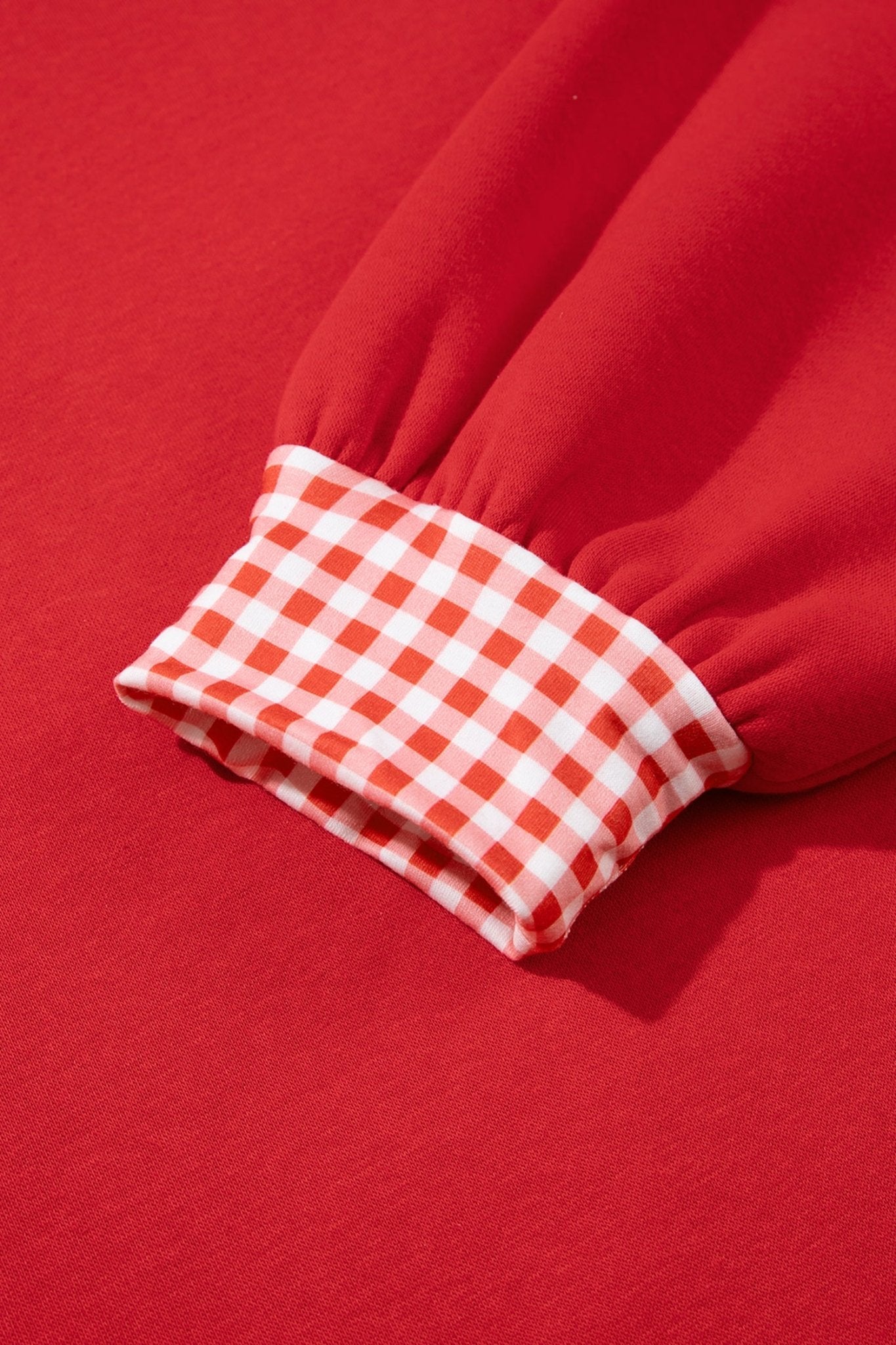 Close-up of red garment sleeve with gathered cuff featuring red-white gingham checks on red background.