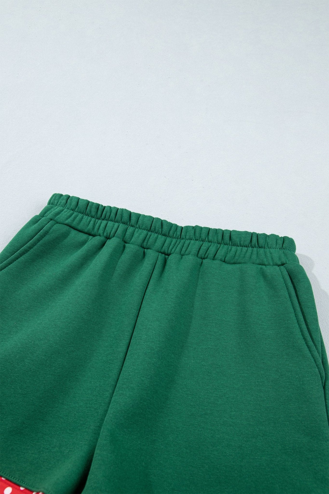 Close-up of green sweatpants showing elastic waistband and side pocket area against a plain light background.