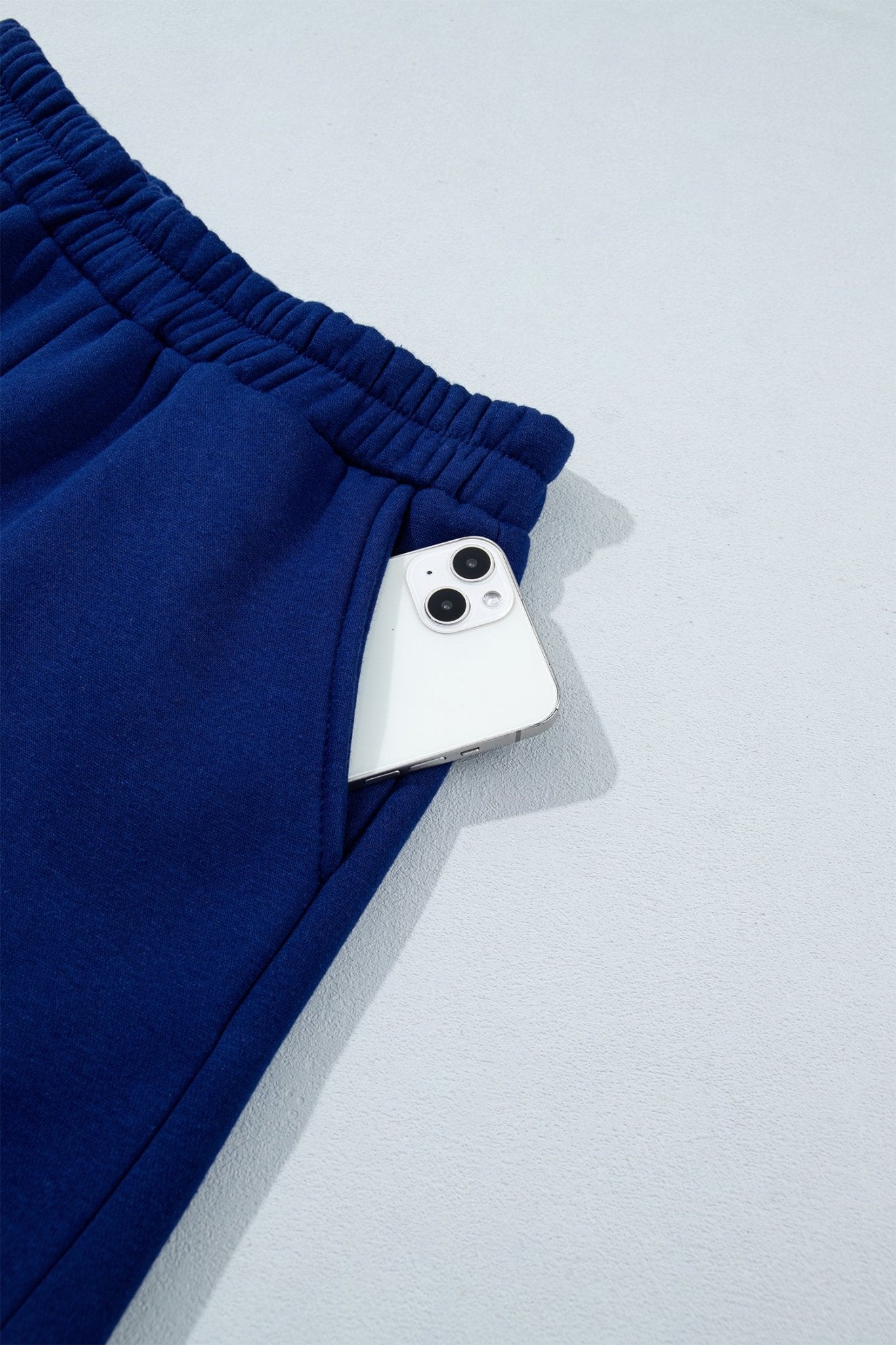 Close-up of royal blue sweatpants with elastic waistband and white smartphone in side pocket.
