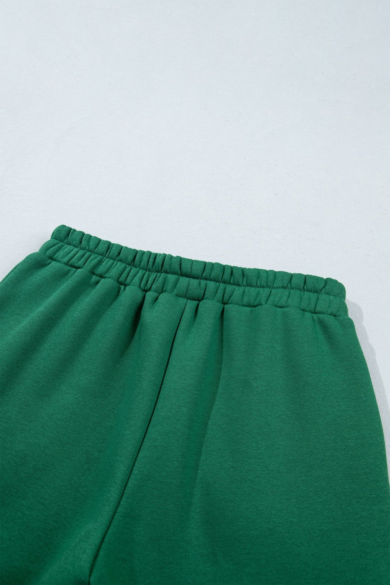 Close-up of green sweatpants showing elastic waistband and upper leg area against a light background.
