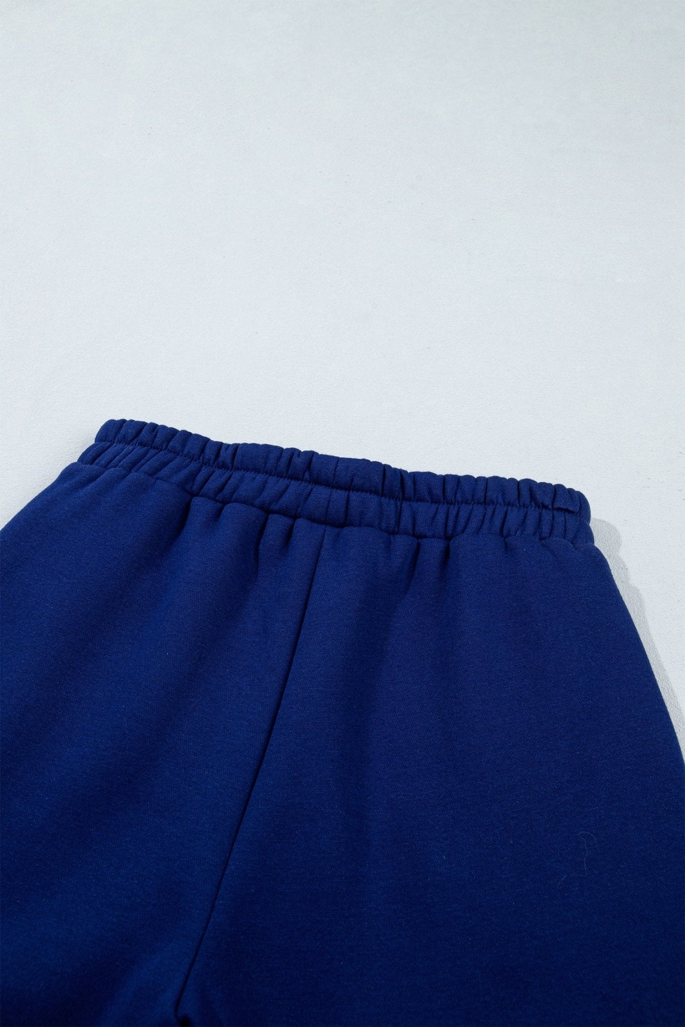 Close-up of a pair of dark blue sweatpants with an elastic waistband, shown against a light gray background.