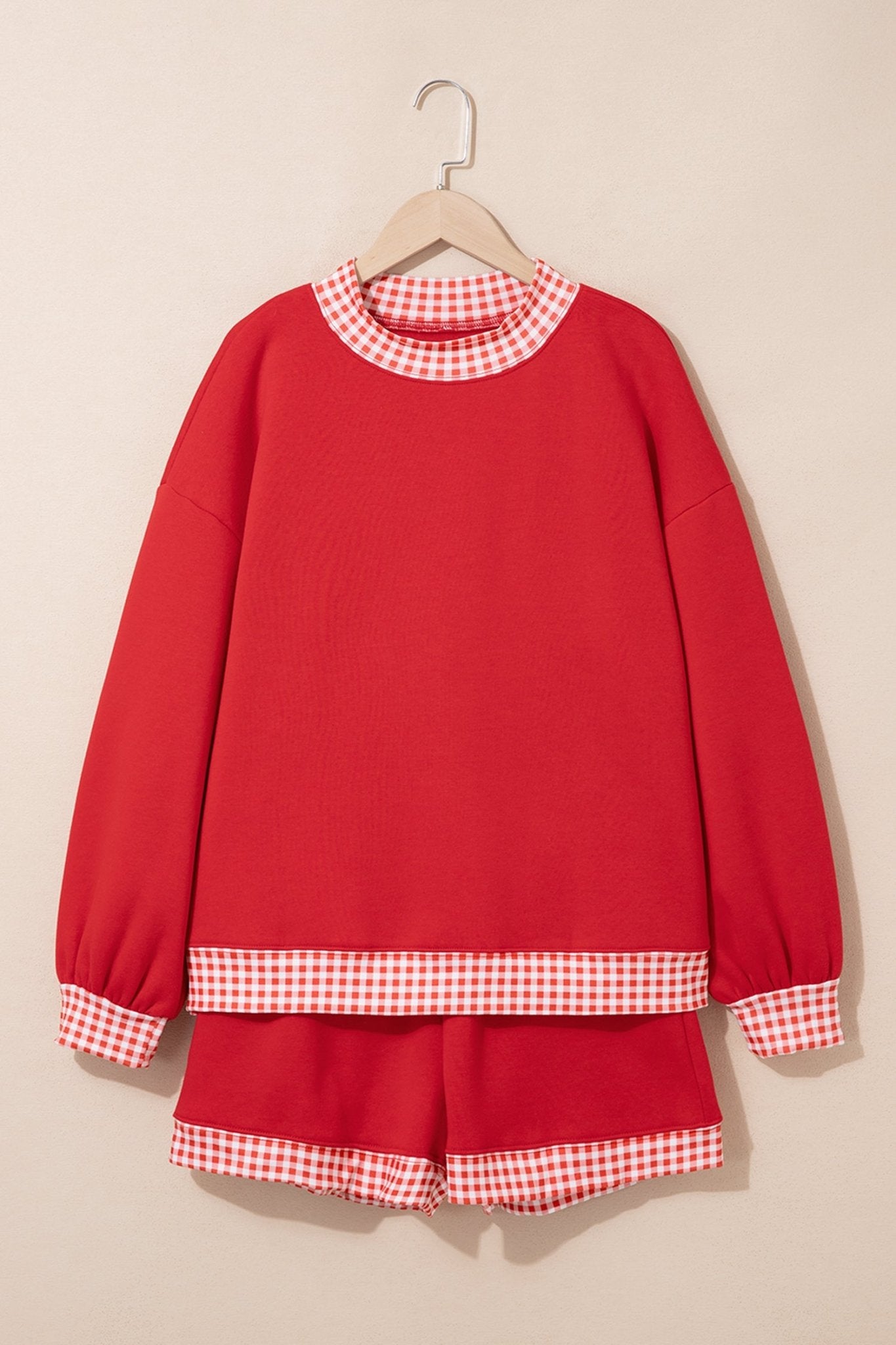 Red long-sleeve sweatshirt and matching shorts set with red-white gingham trim, hanging on a wooden hanger.