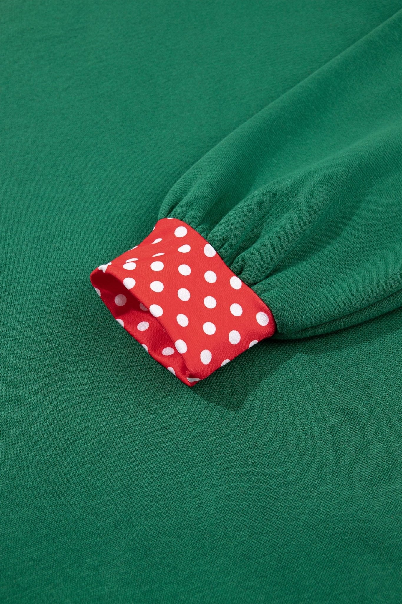Close-up of green knit garment cuff with red-white polka-dot lining against matching green fabric background.