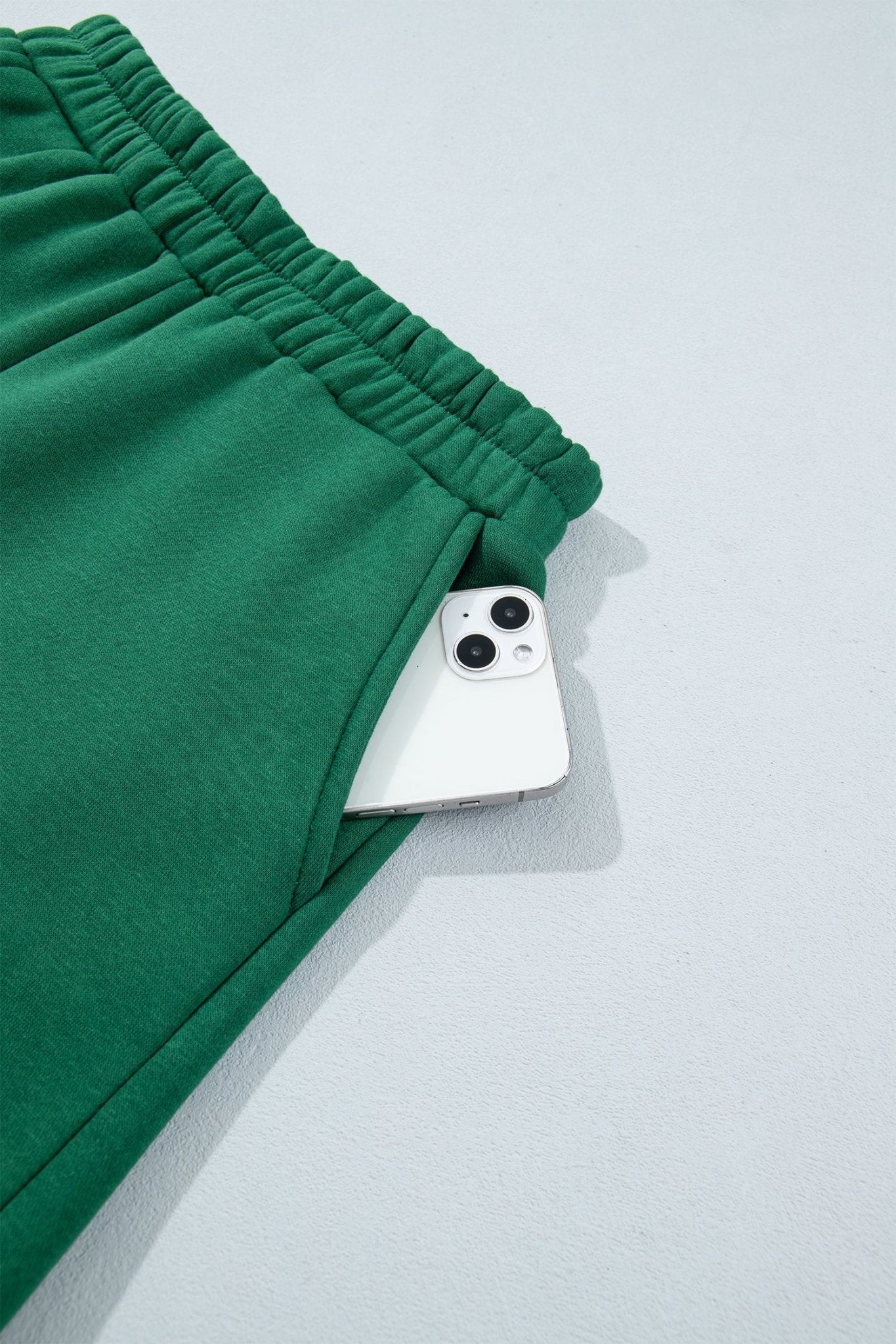 Close-up of green sweatpants with elastic waistband and white smartphone tucked into the side pocket.