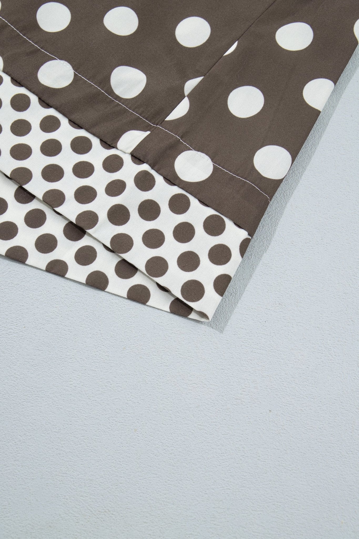 A close-up of folded fabric with a brown and white polka dot pattern, laid on a light gray surface.