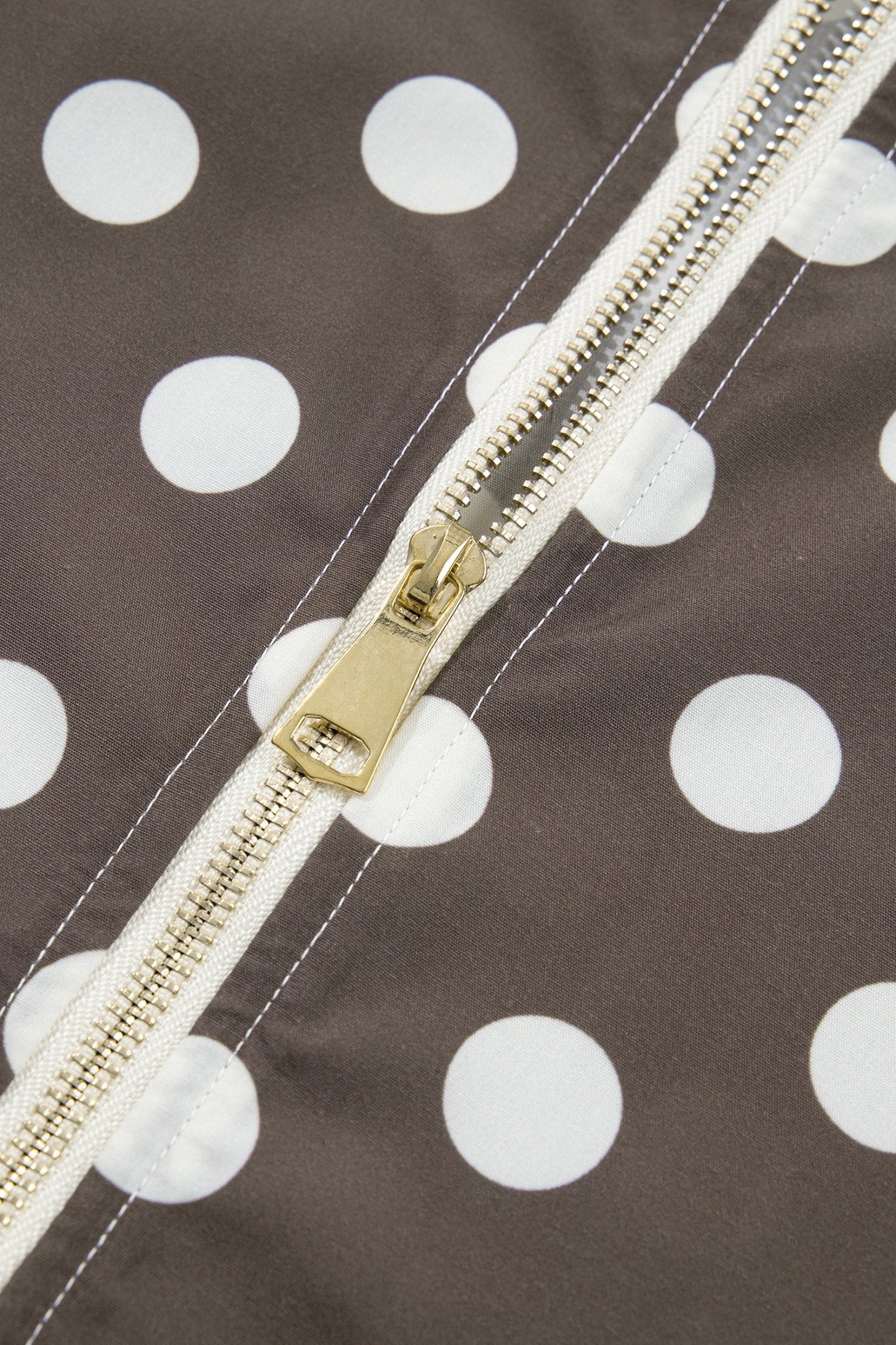 Close-up of a brown fabric with a white polka dot pattern and a gold-toned zipper
