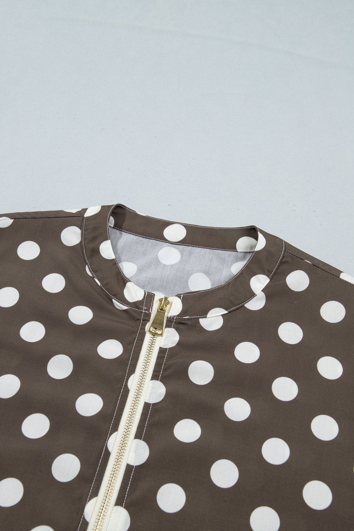 Close-up of a brown and white polka dot garment with a gold zipper, showing the collar