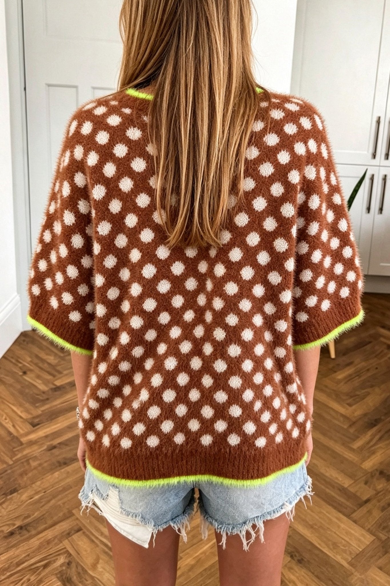 Back view of woman in brown polka-dot sweater with lime trim and denim shorts.