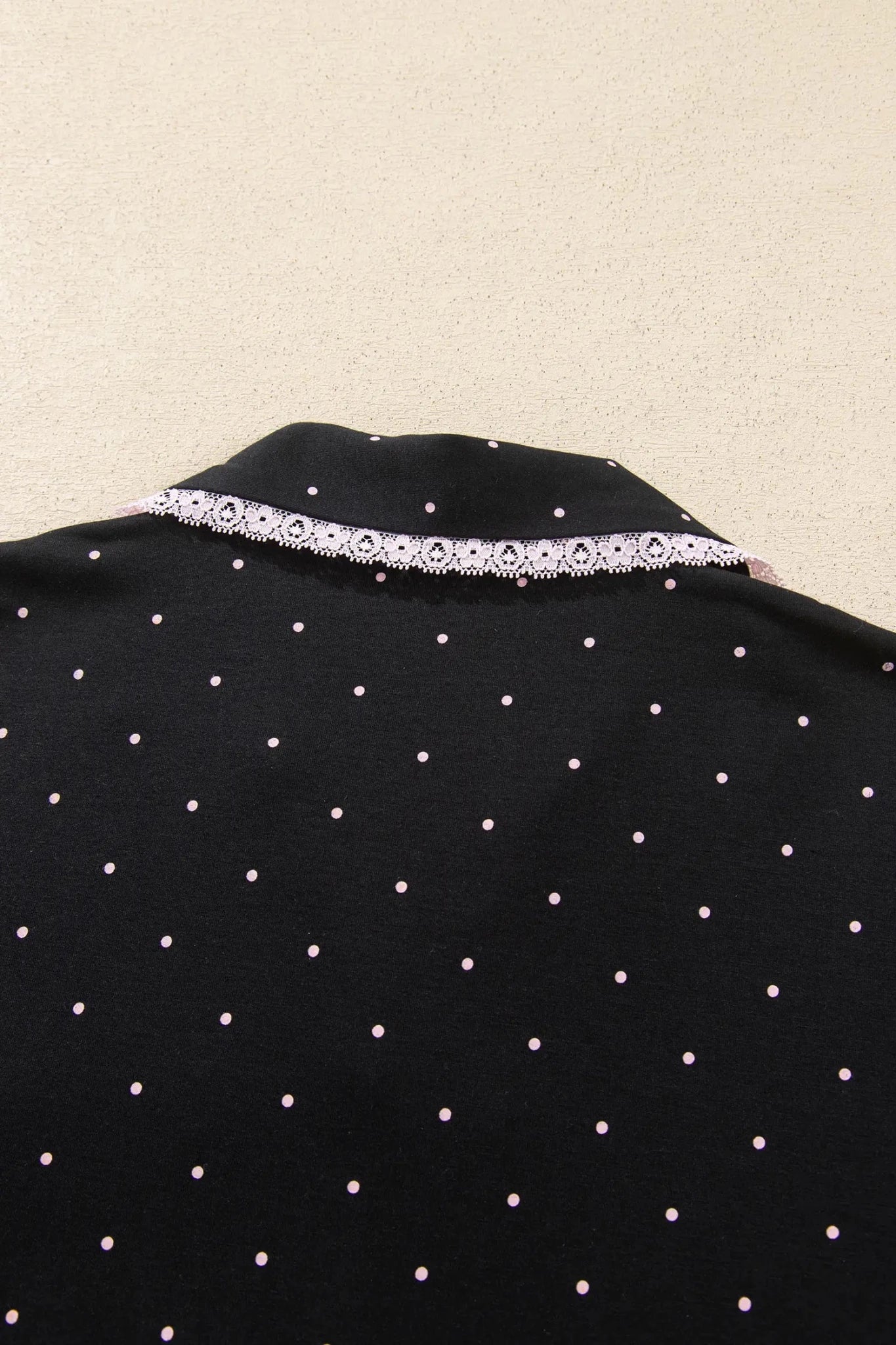 Close-up of black fabric with pink polka dots and white lace neckline trim.