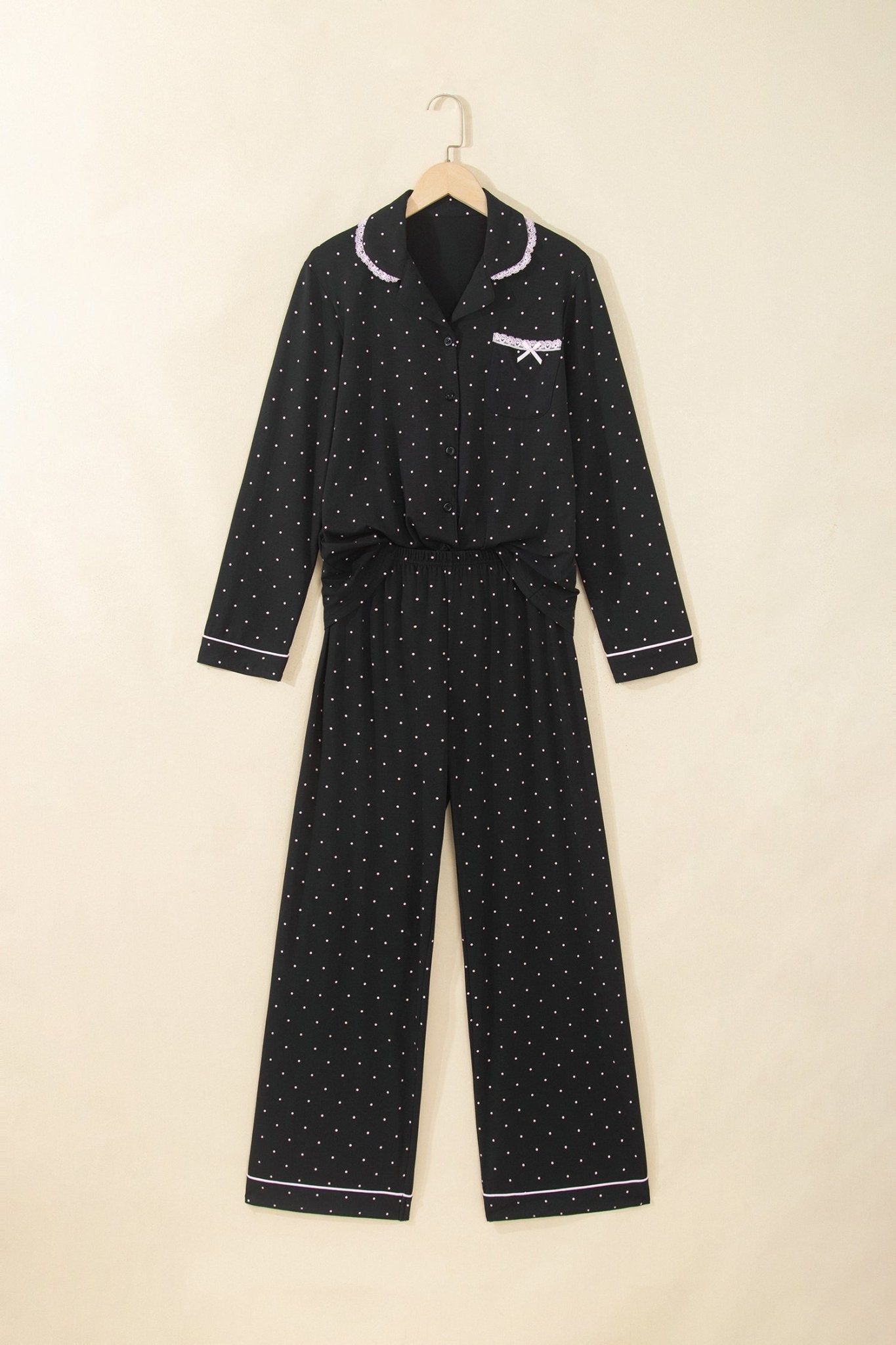 Black polka-dot pajamas with white piping, waist tie, and chest bow on hanger.