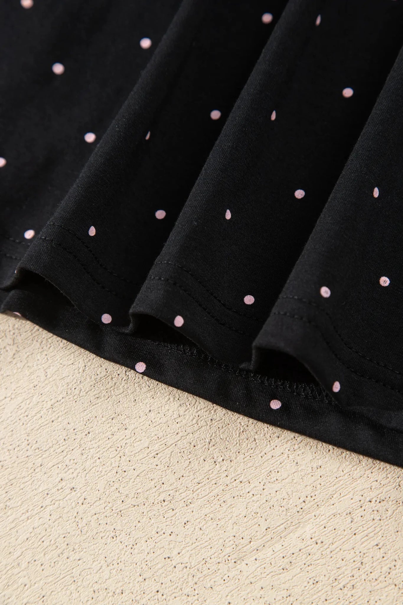 Close-up of black fabric with pink polka dots, folded on beige surface.