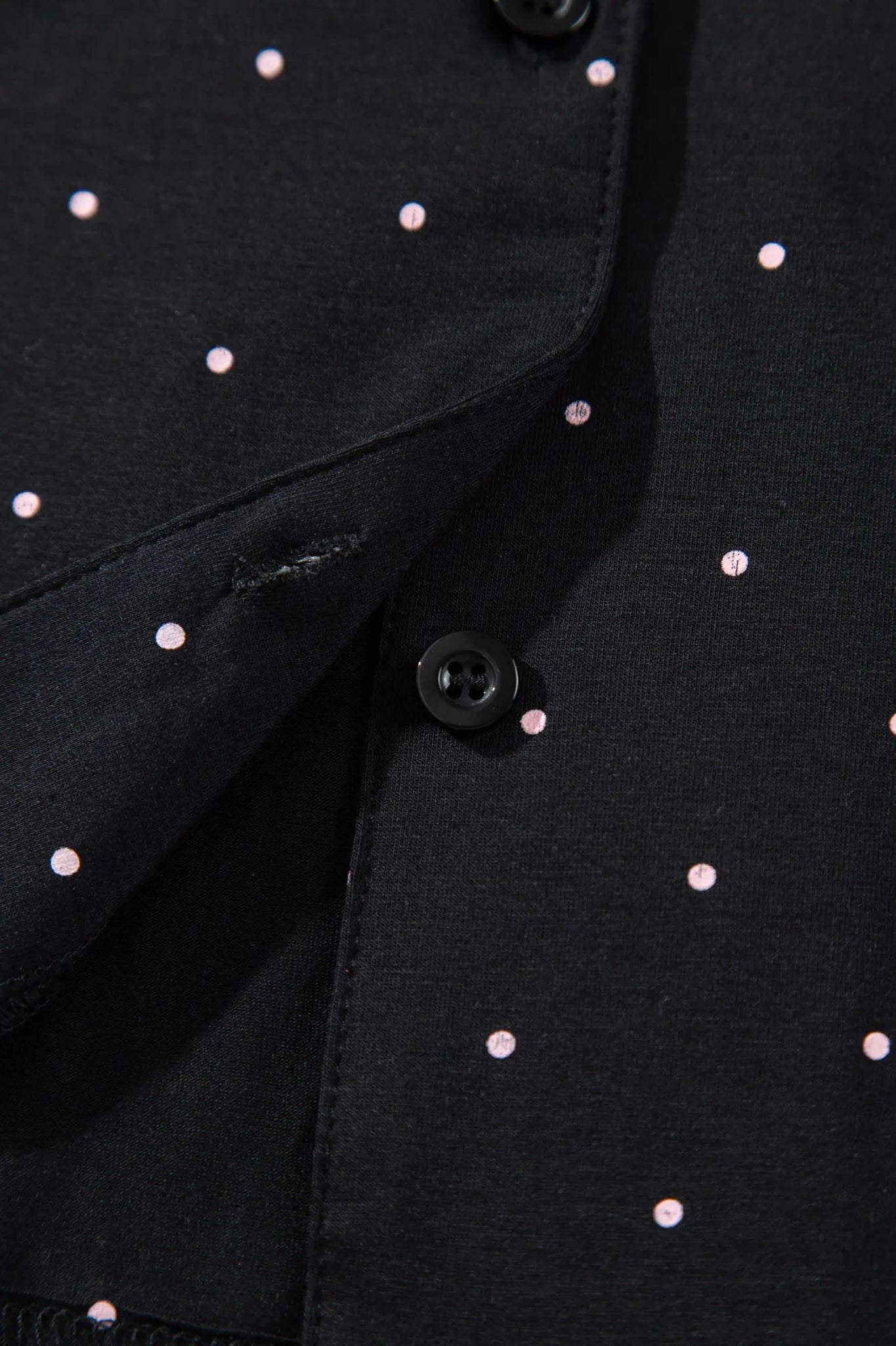Close-up of black button-front garment with pink polka dots and folded cuff.