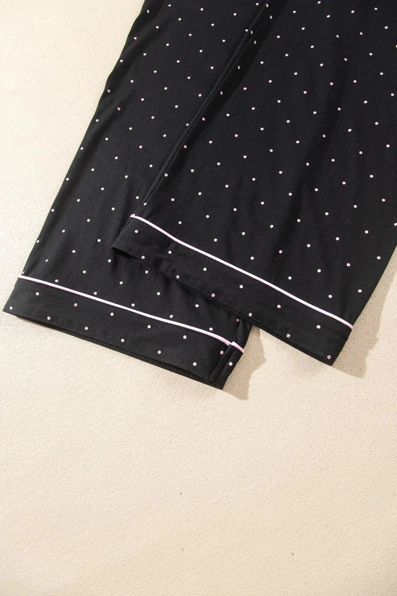 Black pajama pants with white polka dots and piping cuffs, laid flat.