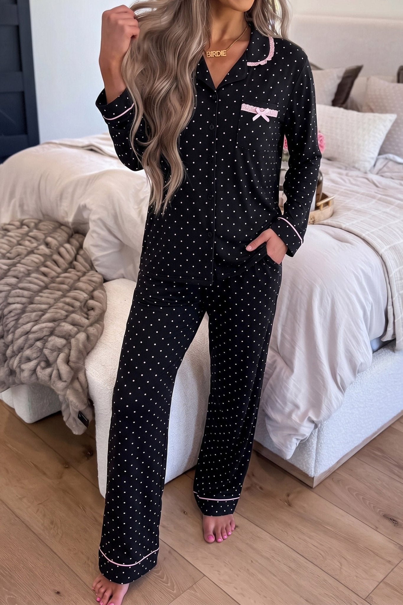 Woman in black polka-dot pajamas with light pink trim in bedroom.