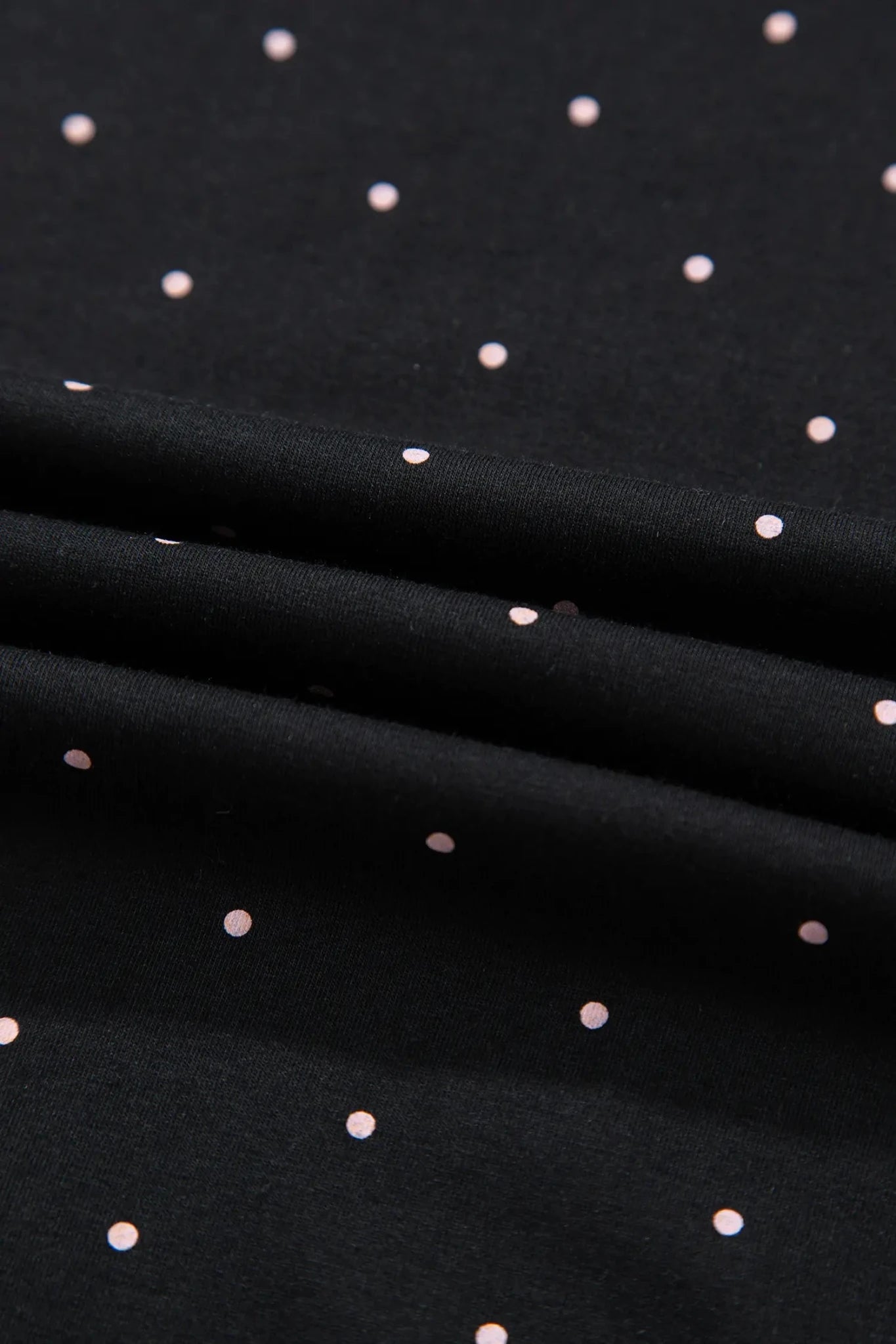 Black fabric with a scattered pattern of small metallic rose gold dots, shown with soft folds.