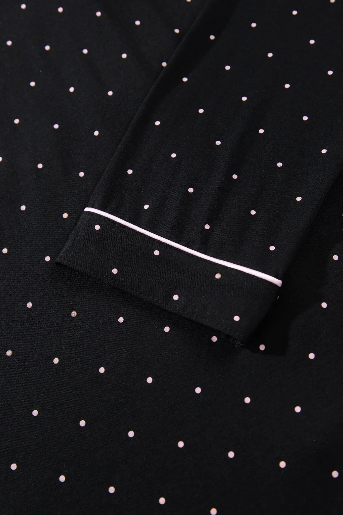 Close-up of black fabric with white polka dots and white cuff piping.