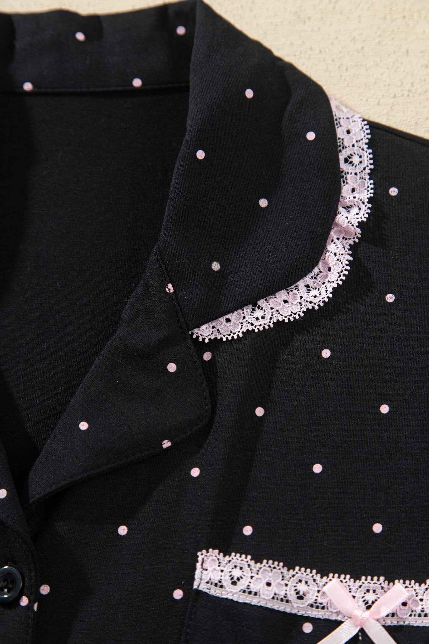 Close-up of black polka-dot garment with pink lace trim and bow detail.