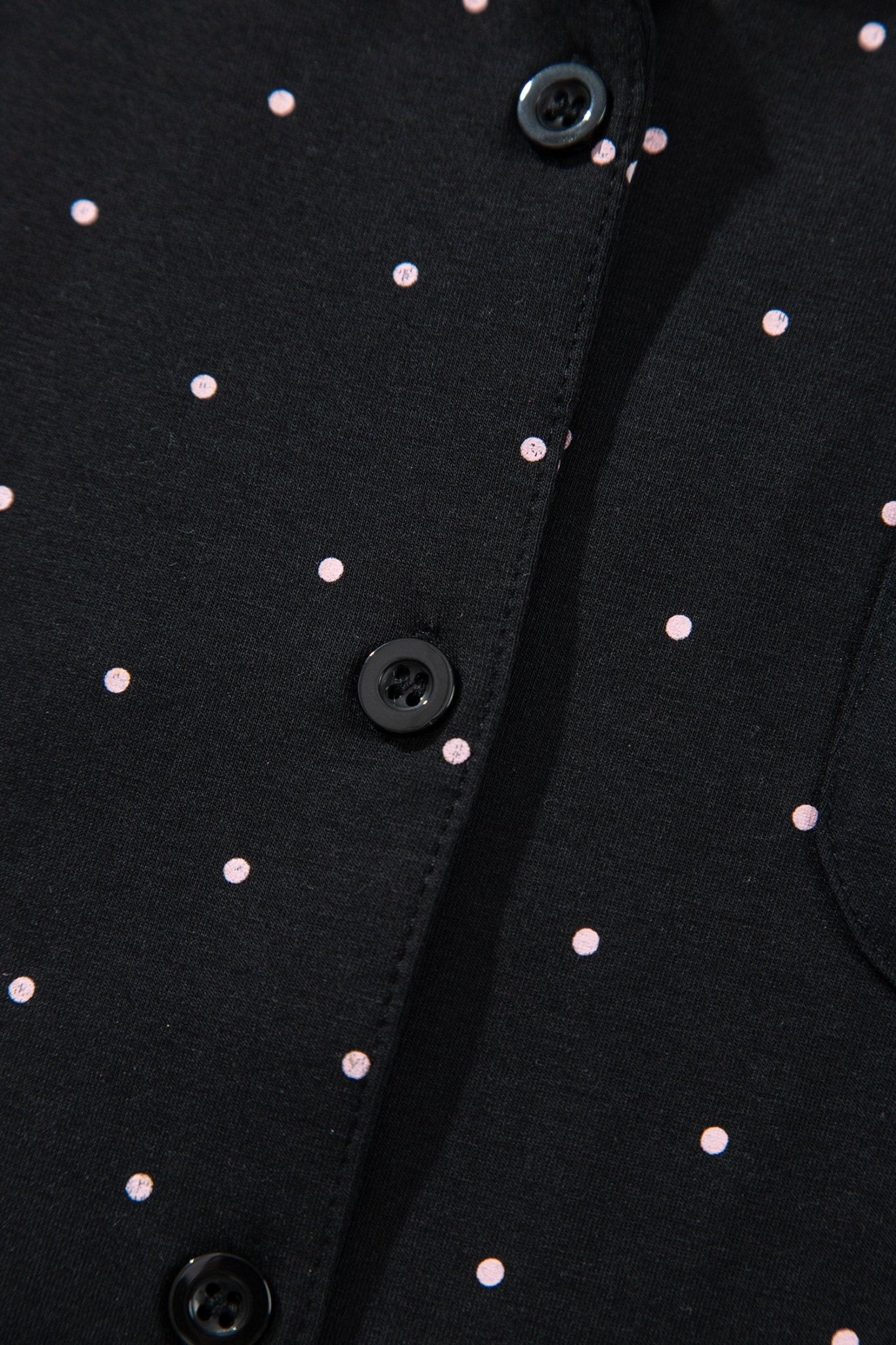 Close-up of a black button-front garment with small evenly spaced light pink polka dots and dark buttons.