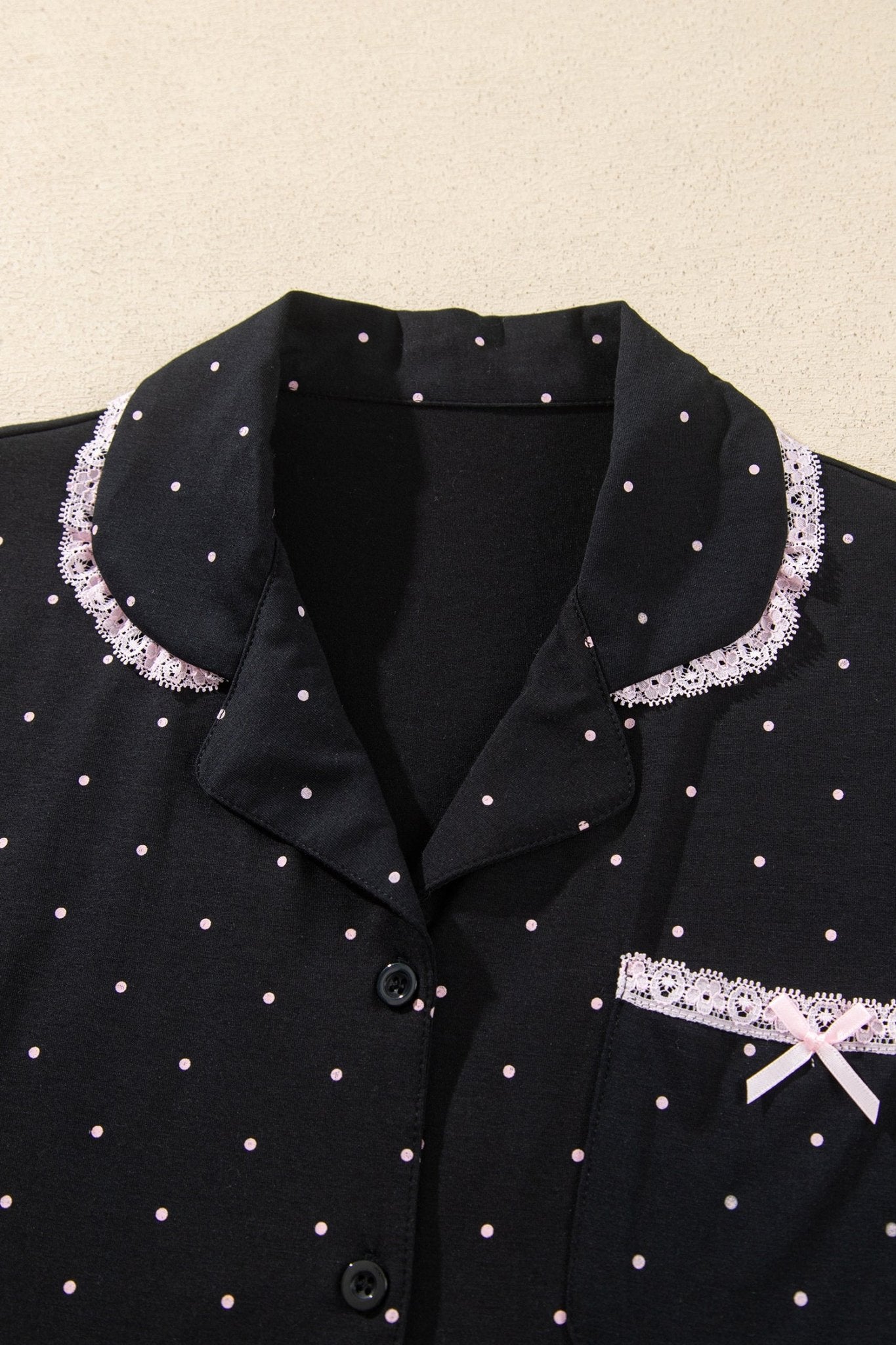 Black pajama top with pink polka dots, lace collar, pocket trim, and bow.