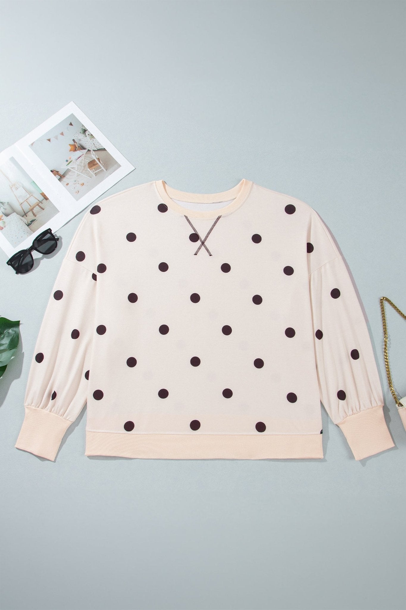 Flat lay of light peach-beige brown-dot crewneck sweatshirt with sunglasses & gold chain on gray.