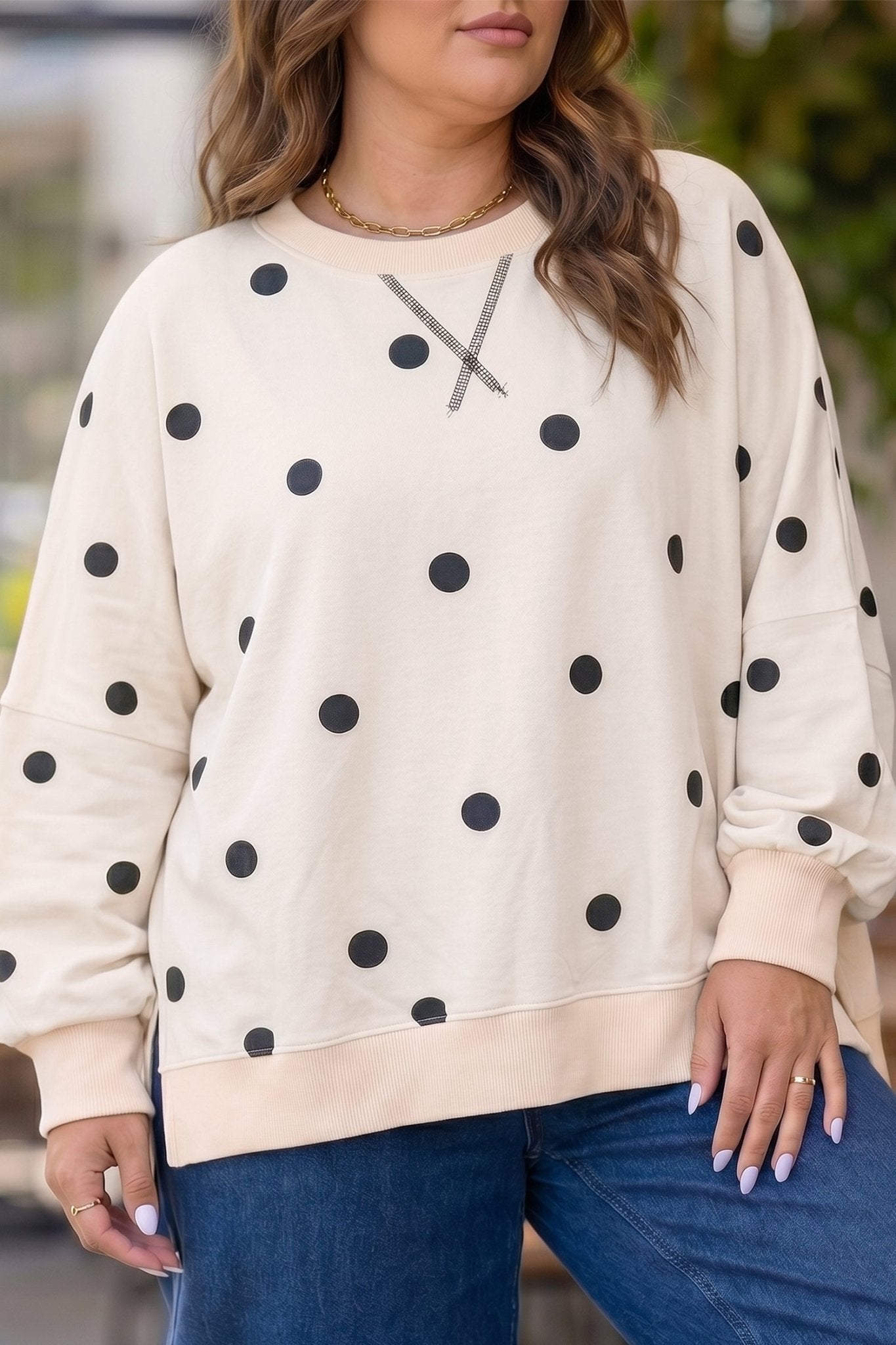 Woman in cream black-polka-dot crewneck with gray chest line & jeans.