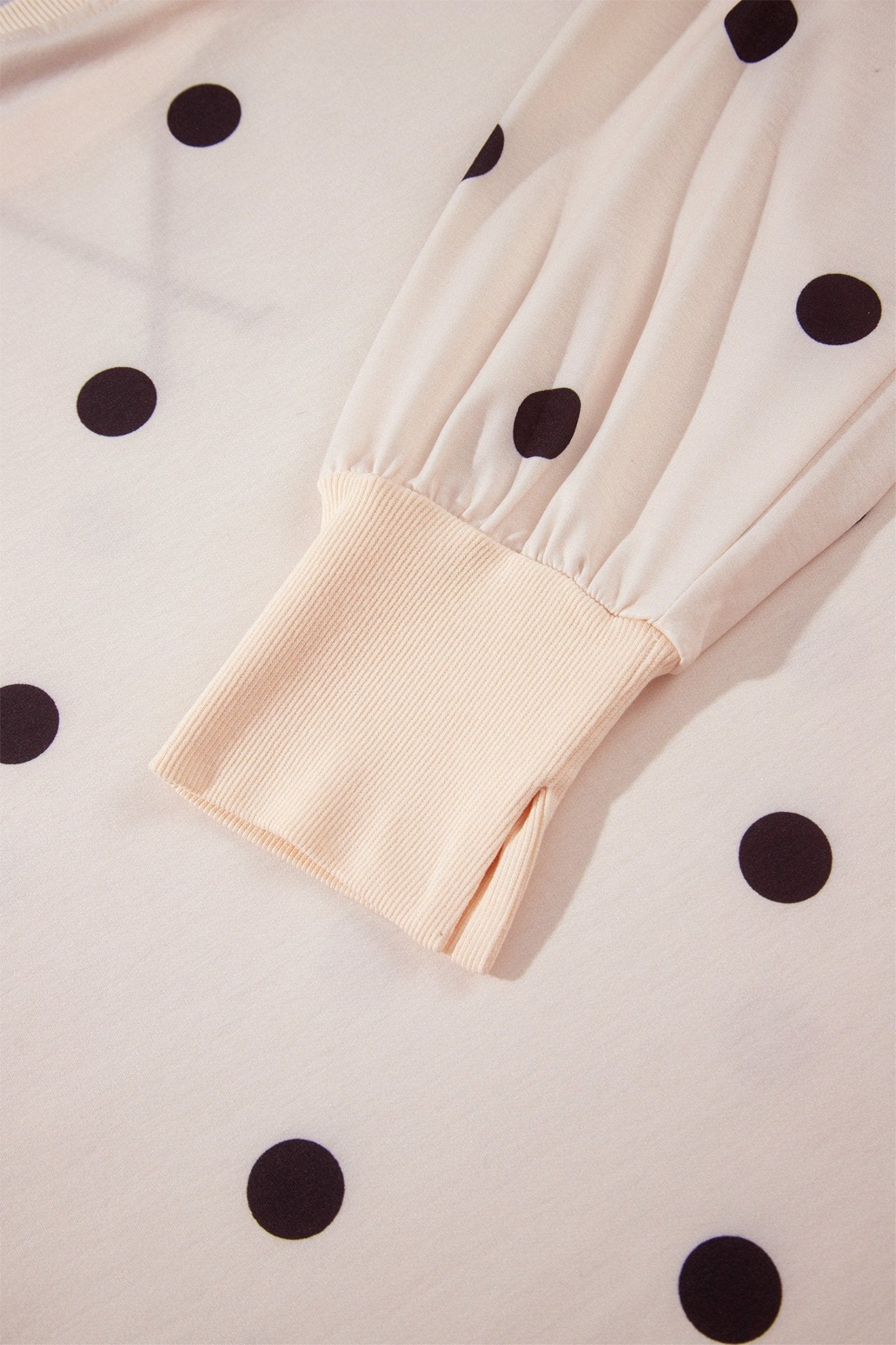 Close-up of cream long-sleeve blouse with black polka dots and ribbed cuff on matching fabric.