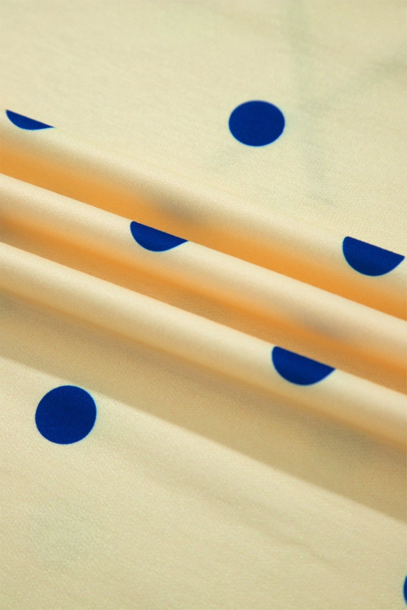 A close-up of cream-colored fabric with a pattern of dark blue polka dots, draped diagonally with soft shadows.