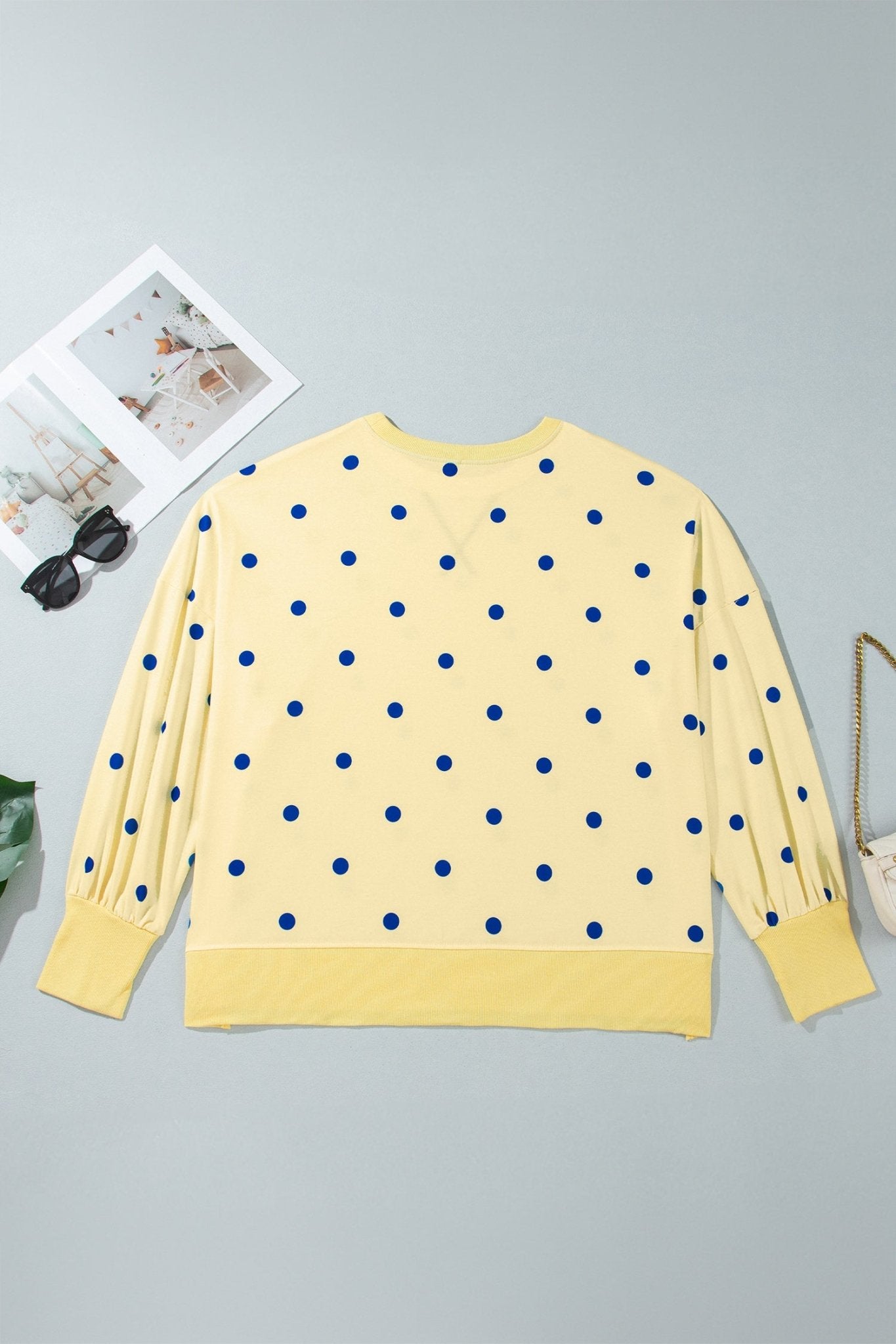 Flat lay back view of pale yellow blue-dot sweatshirt with sunglasses, magazine & purse.