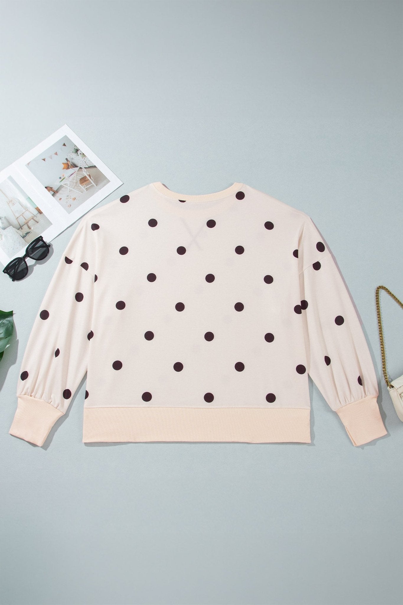 Flat lay of light peach-beige brown-dot crewneck sweatshirt with decorative props on gray background.