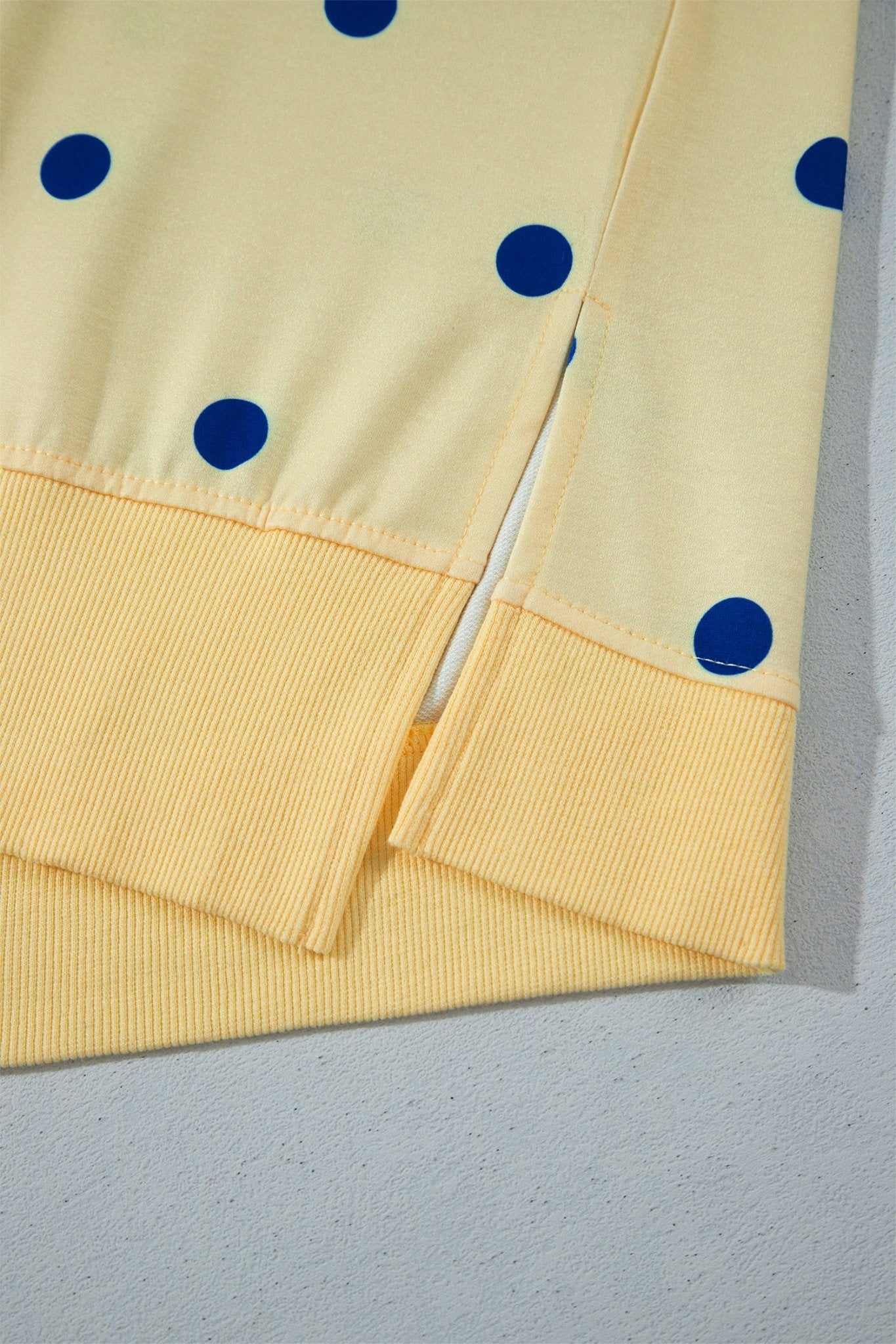 Close-up of a pale yellow garment with blue polka dots and ribbed cuffs, laid flat on a light gray surface.