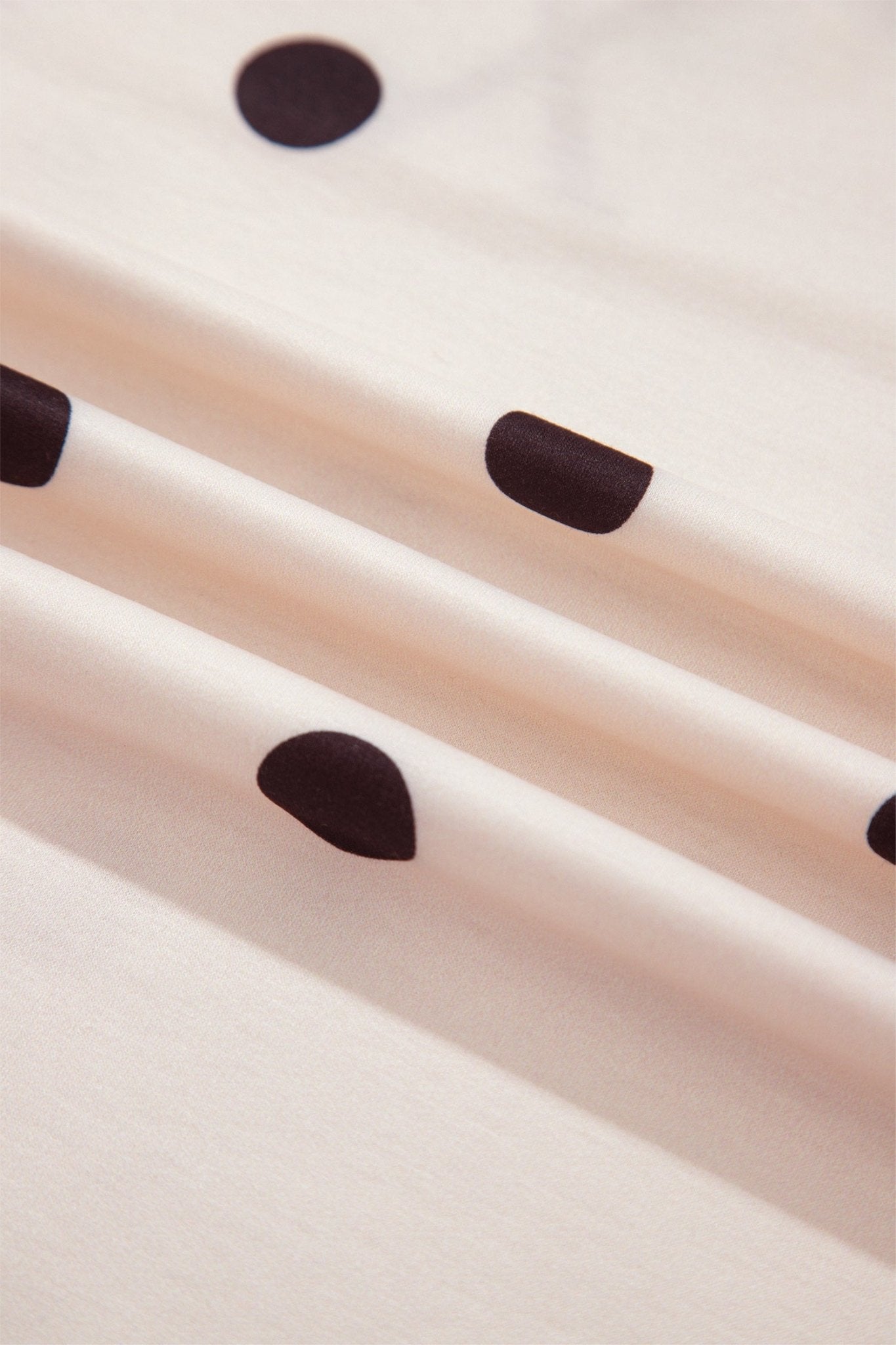 Close-up of a cream-colored fabric or material with dark brown polka dots and diagonal stripes.