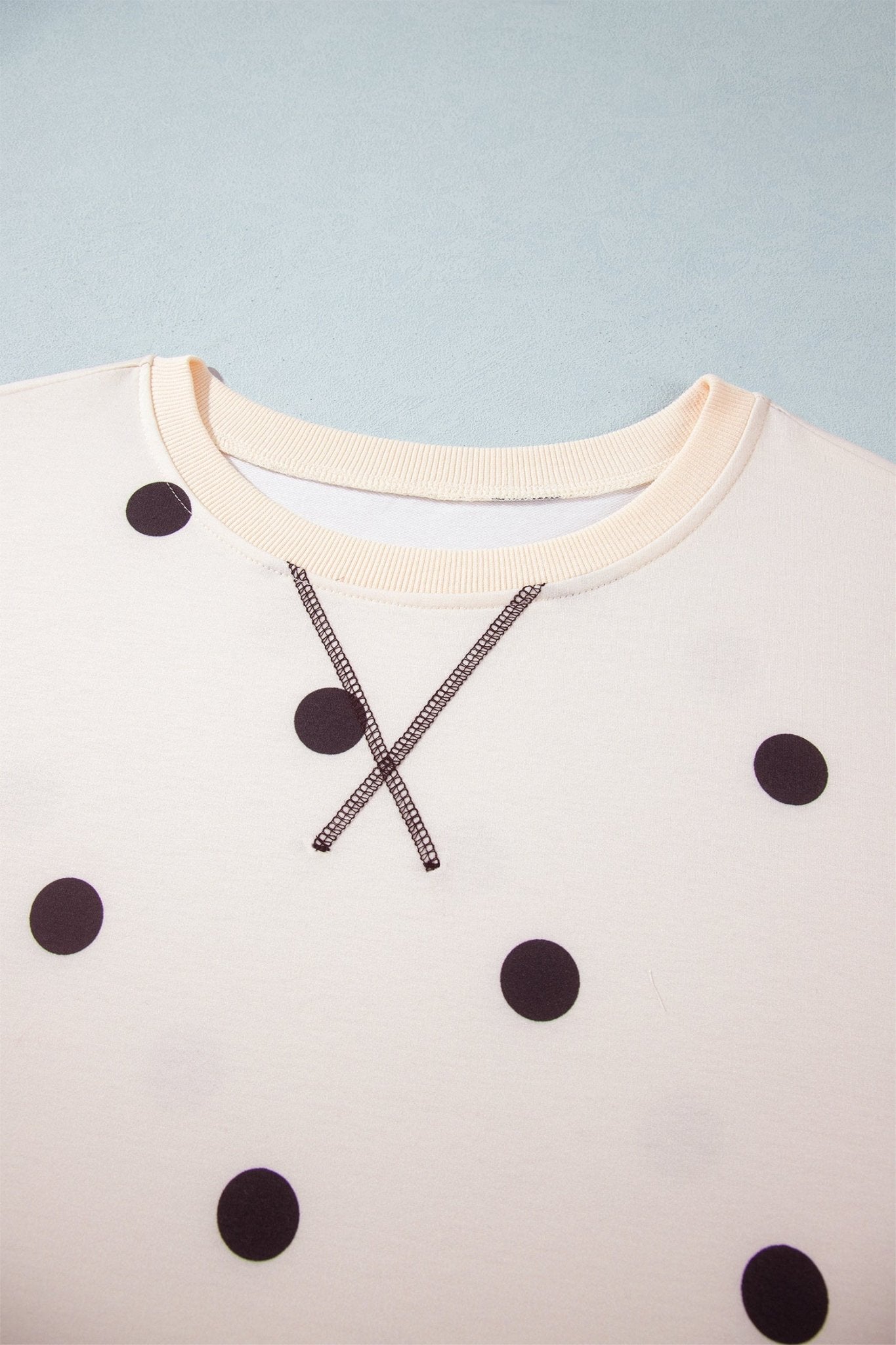 Close-up of cream crewneck sweatshirt with dark brown polka dots and crossed zipper neckline detail.