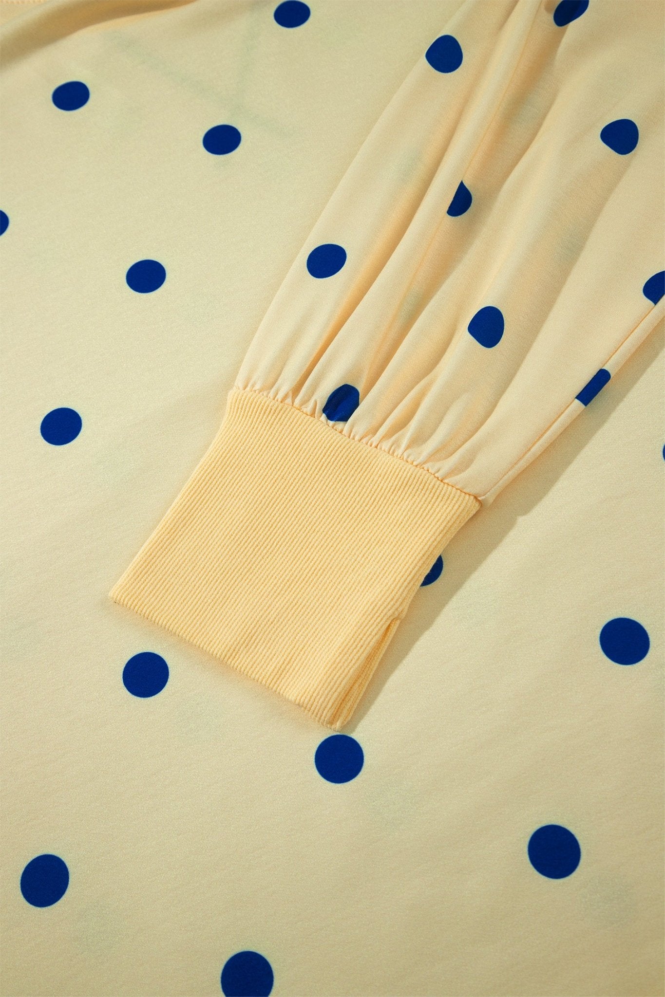Close-up of cream sheer sleeve with dark blue polka dots and ribbed cuff on matching dotted fabric.