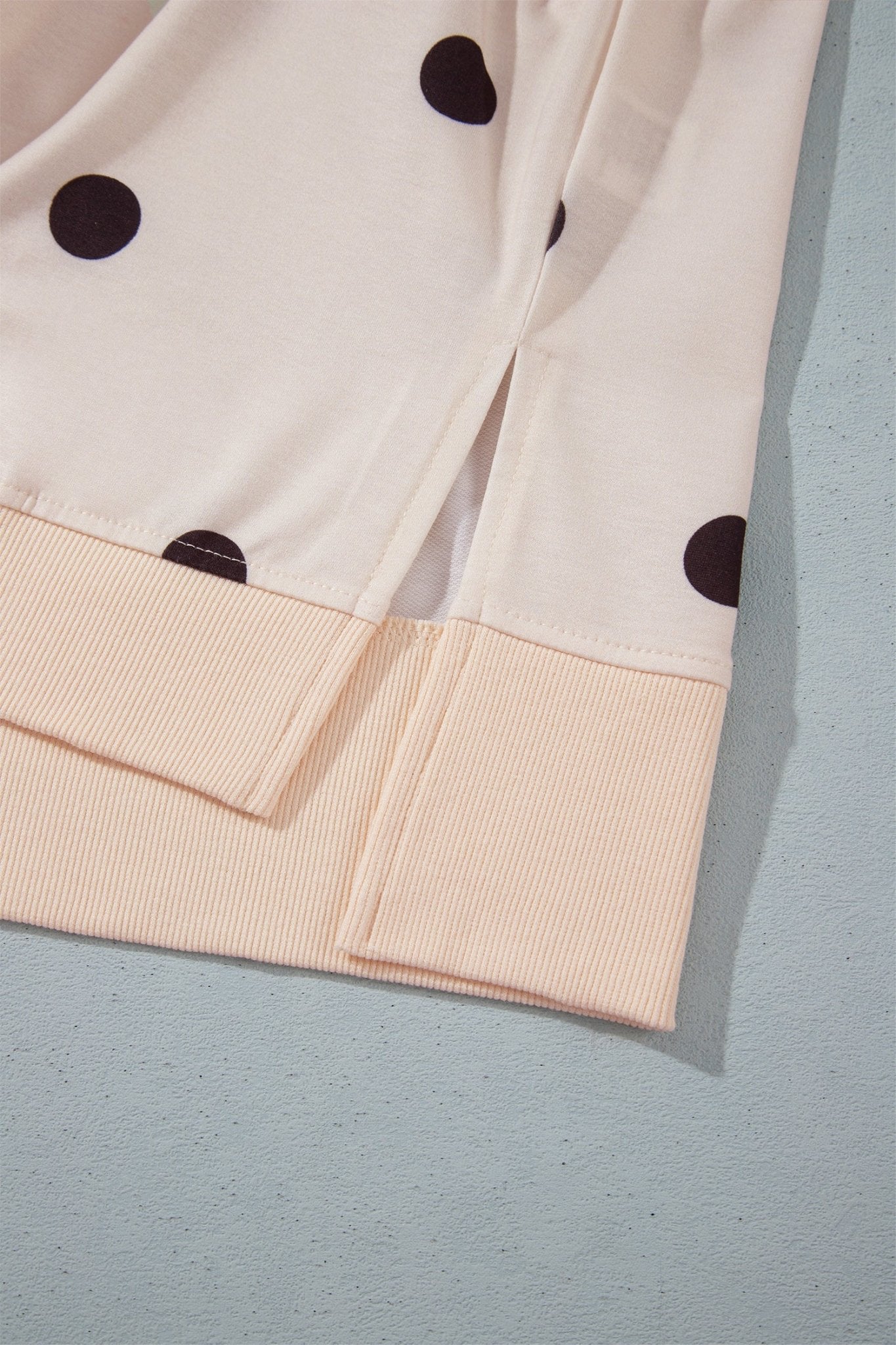 Close-up of cream dark-brown-dot garment with peach-beige ribbed cuff on blue-gray surface.